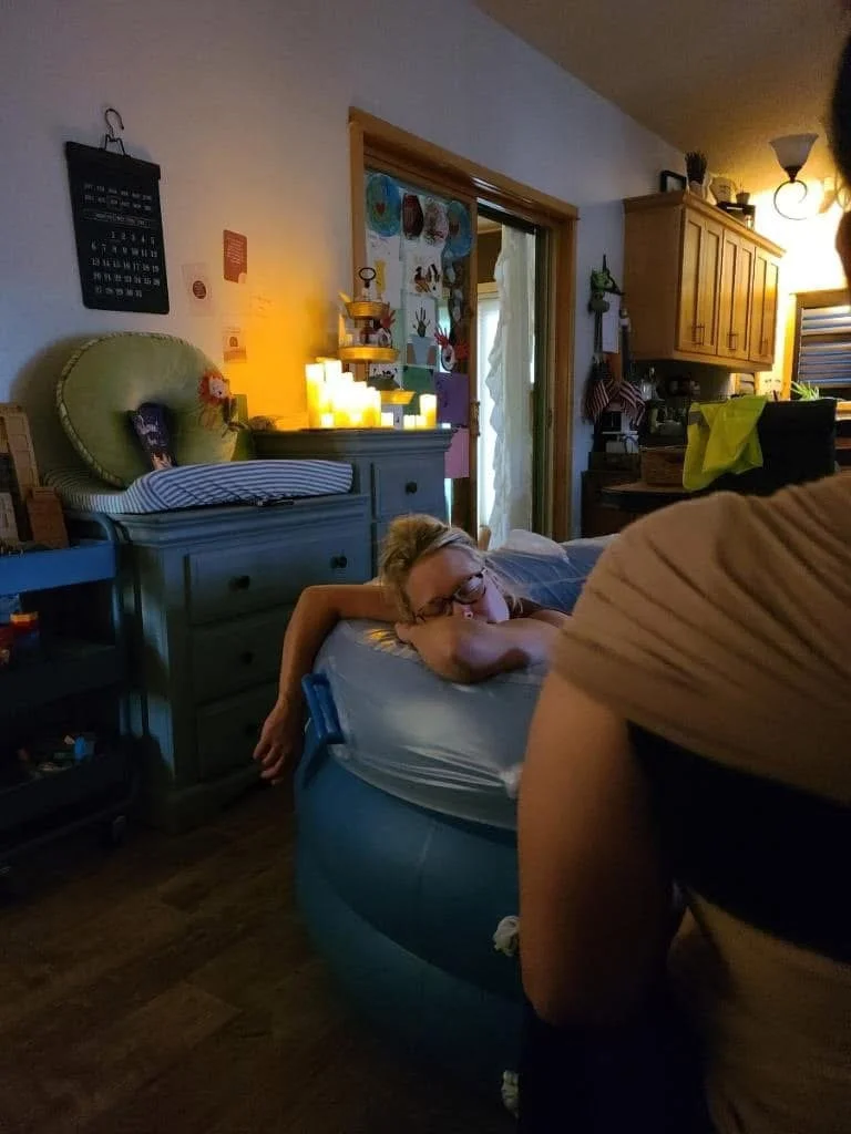 A young girl lying on an inflatable pool float in a cozy living room, with her head resting on her arms and wearing glasses.