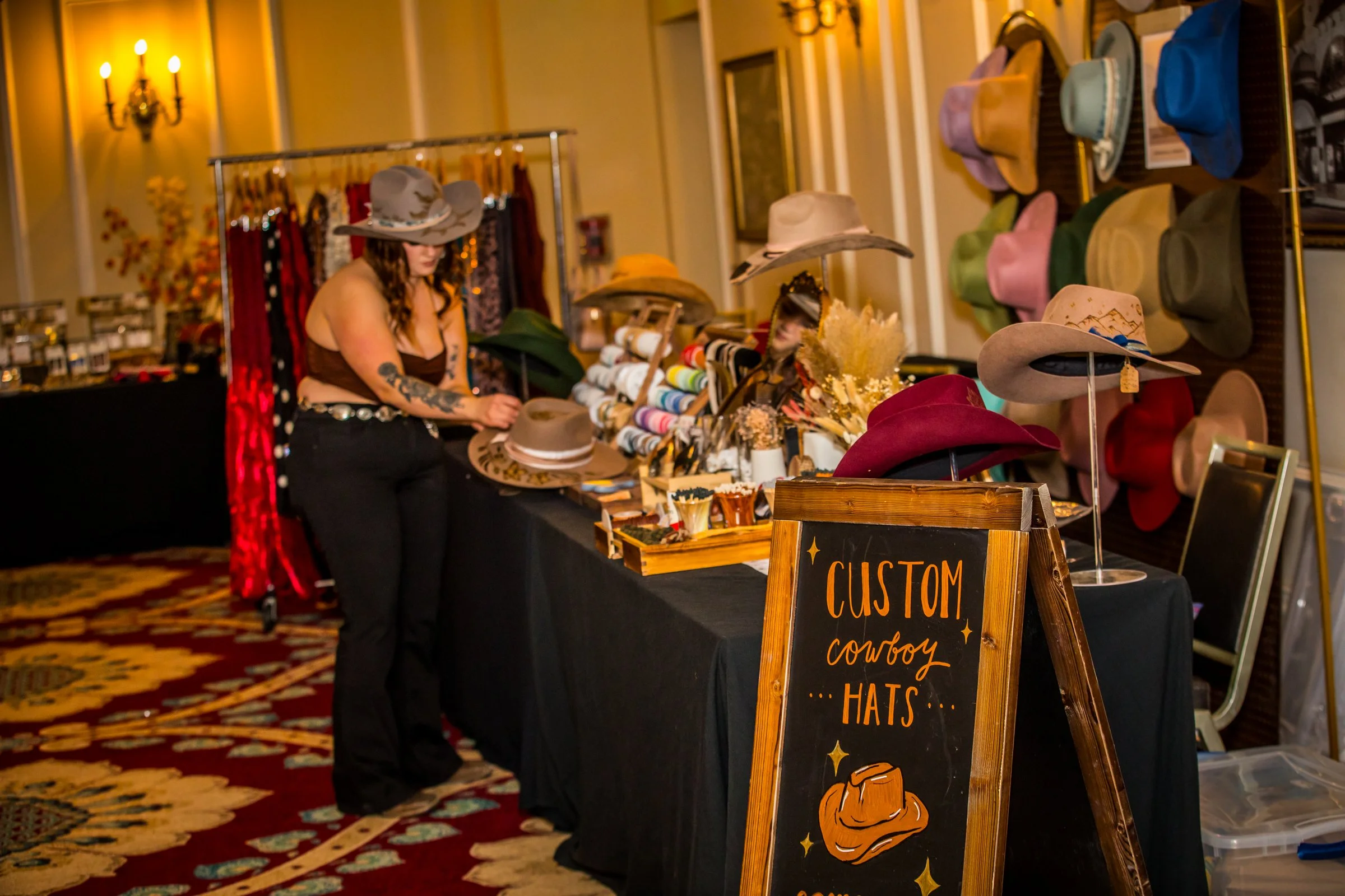 Rachel of Kindled Stitch hand burning a design into a custom hat at her vendor table PC Gabriel (Picture Perfect Visions)