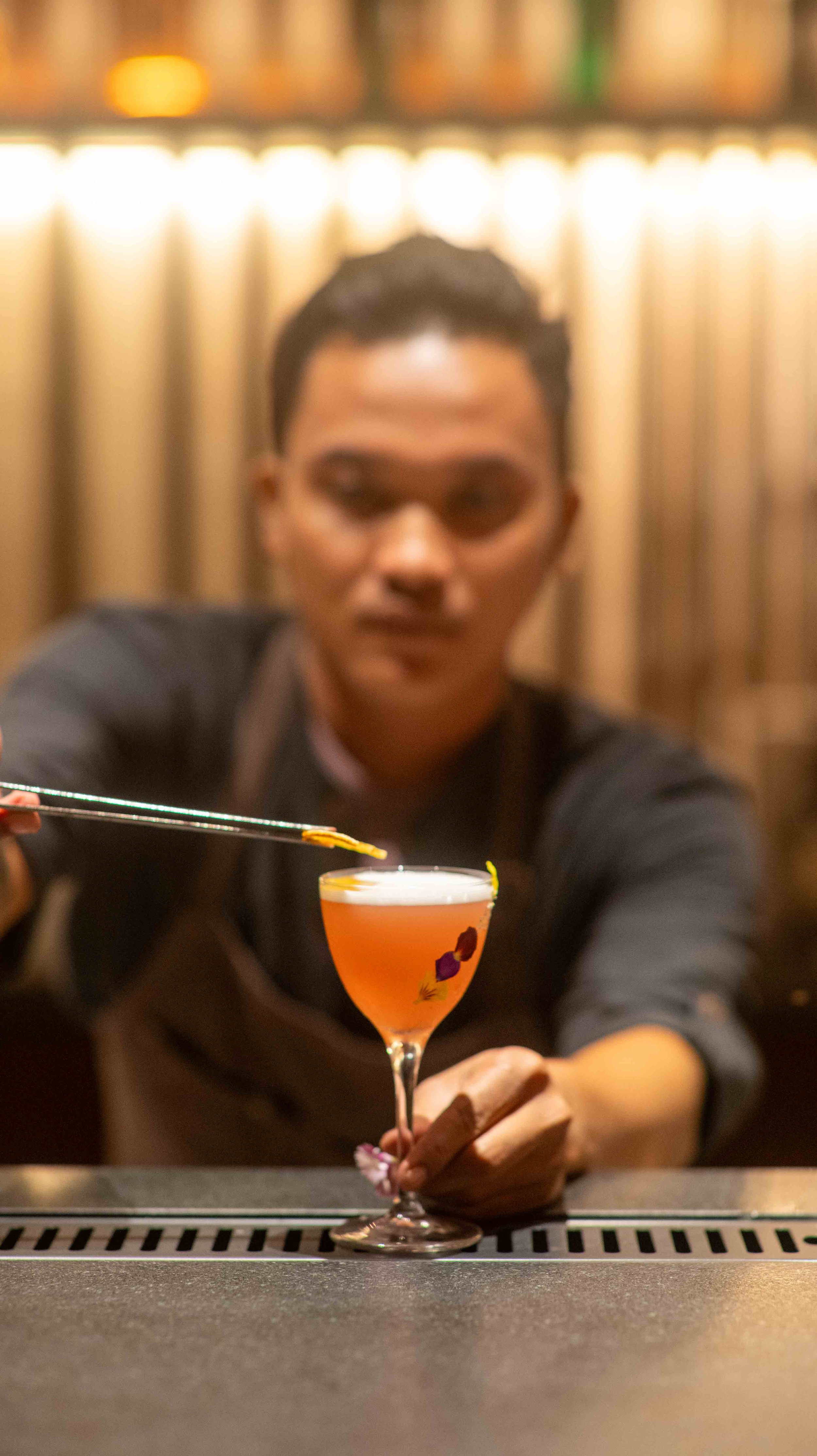 Bartender garnishing a cocktail with tweezers