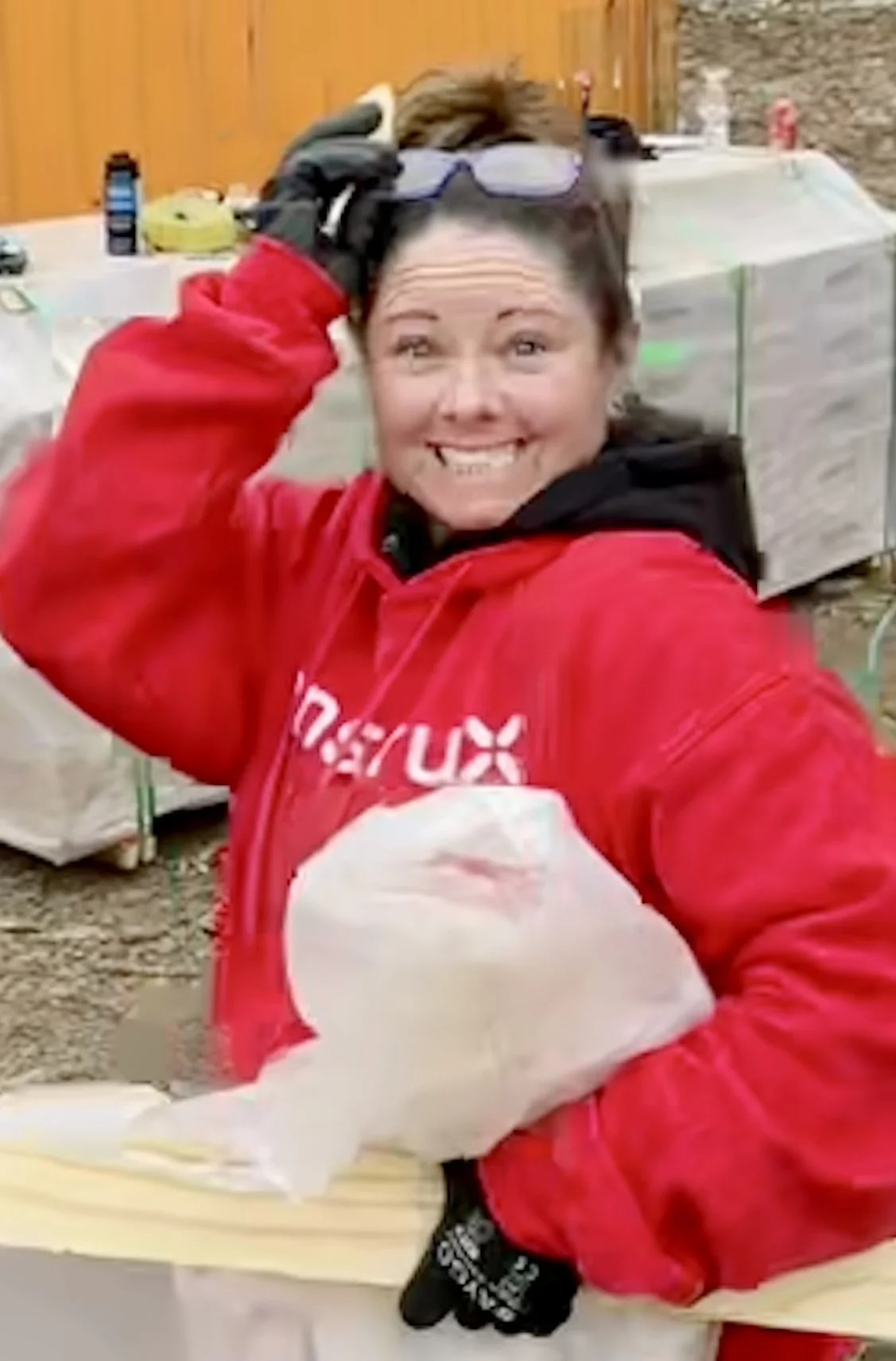 Person wearing a red hoodie and black gloves holding a plastic-wrapped item.