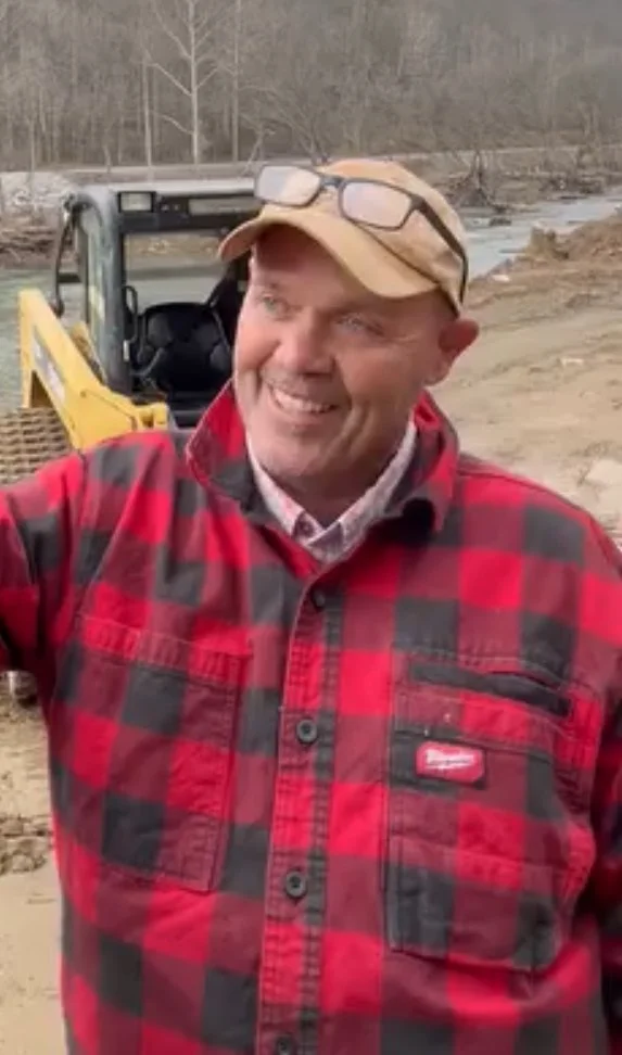 Person in red plaid shirt and tan cap standing outdoors near construction equipment.