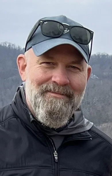 Man with a beard wearing a cap and sunglasses outdoors