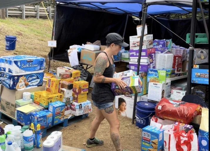 Person organizing supplies under a tent, including toilet paper, towels, and canned goods.