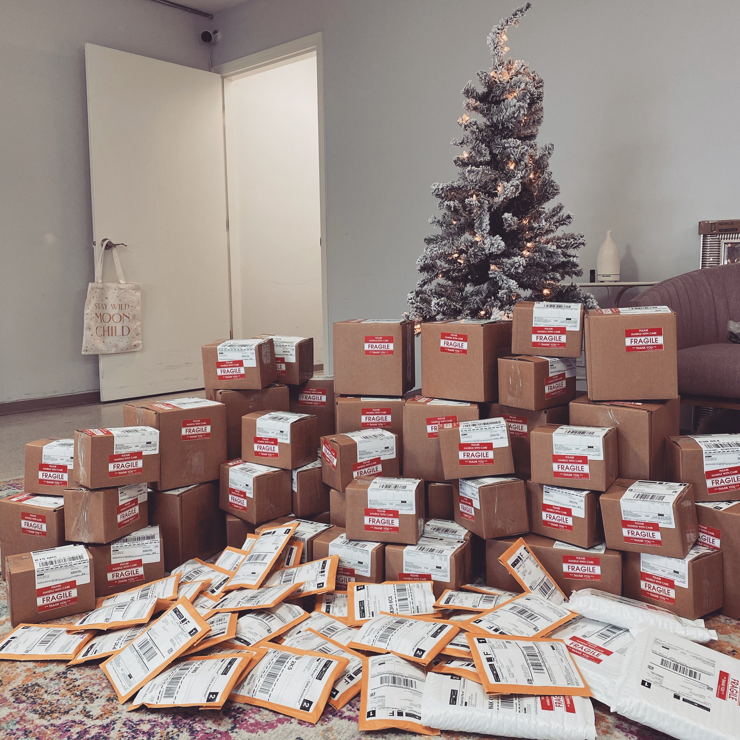 Many packages and envelopes stacked under a small, flocked Christmas tree in a living room.