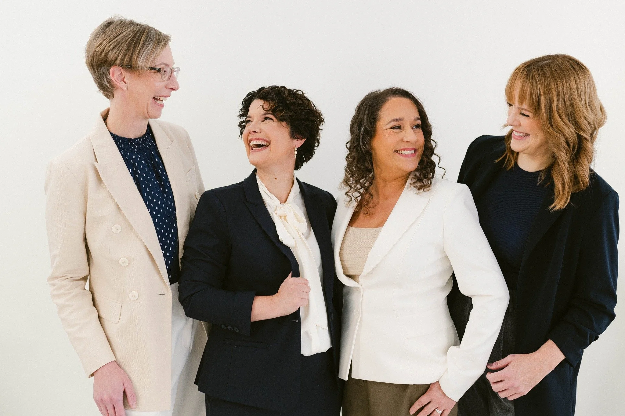 Four women in professional attire laughing and enjoying a conversation.