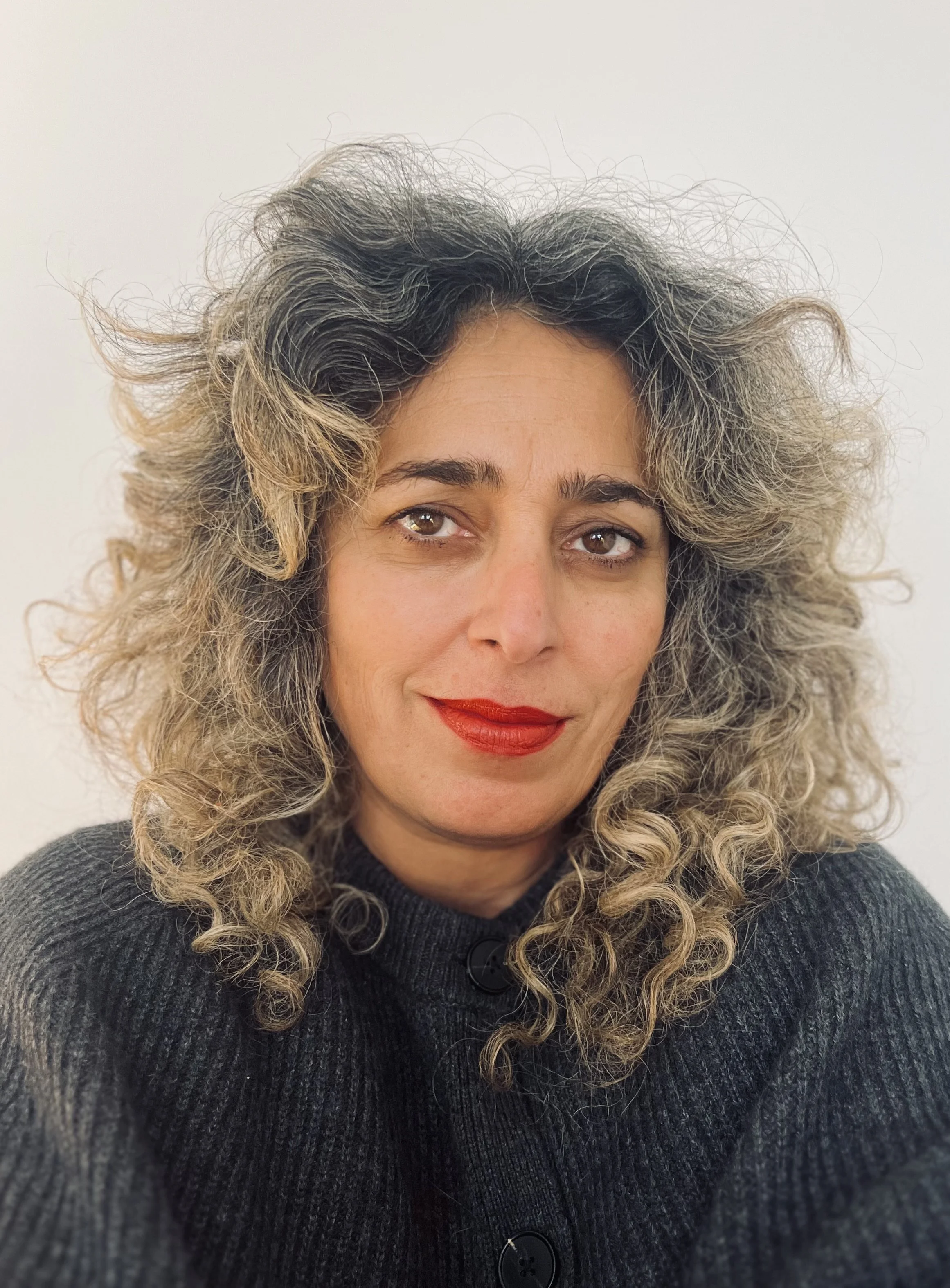 Portrait of a female psychosexual therapist with hair up wearing a black shirt, standing by a window with natural light, conveying warmth, professionalism, and approachability."