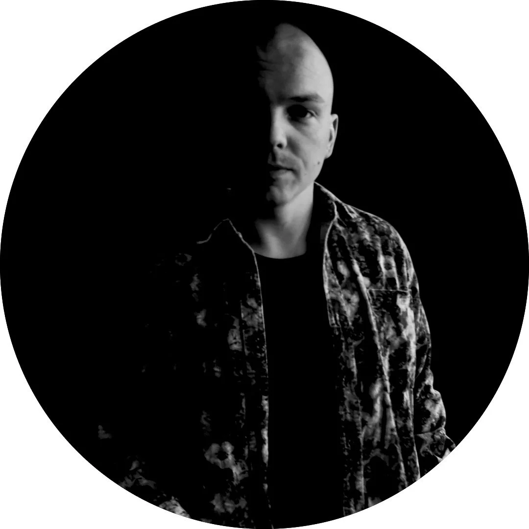 Black and white portrait of a person with one side in shadow, wearing a patterned shirt, against a dark background.