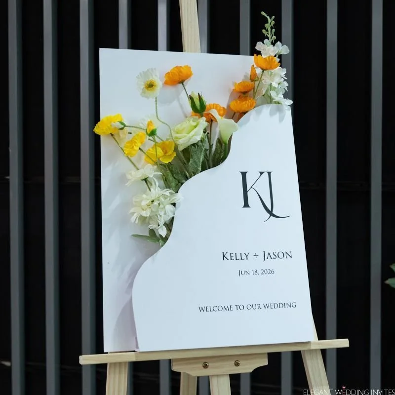 Wedding welcome sign with floral decorations and initials, reading 'Kelly + Jason' and the date 'June 18, 2026' on a wooden easel.