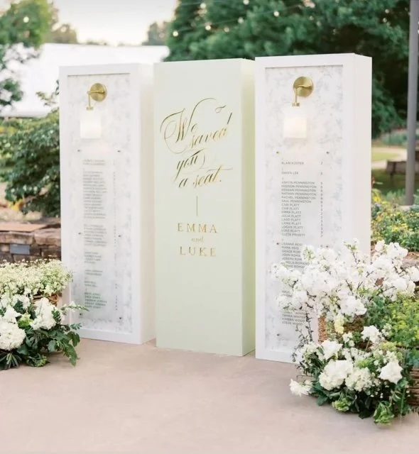 Wedding seating chart with gold lettering and floral arrangements.