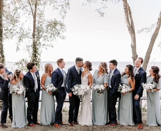 Bride and groom at wedding with wedding party outdoors near water, surrounded by trees