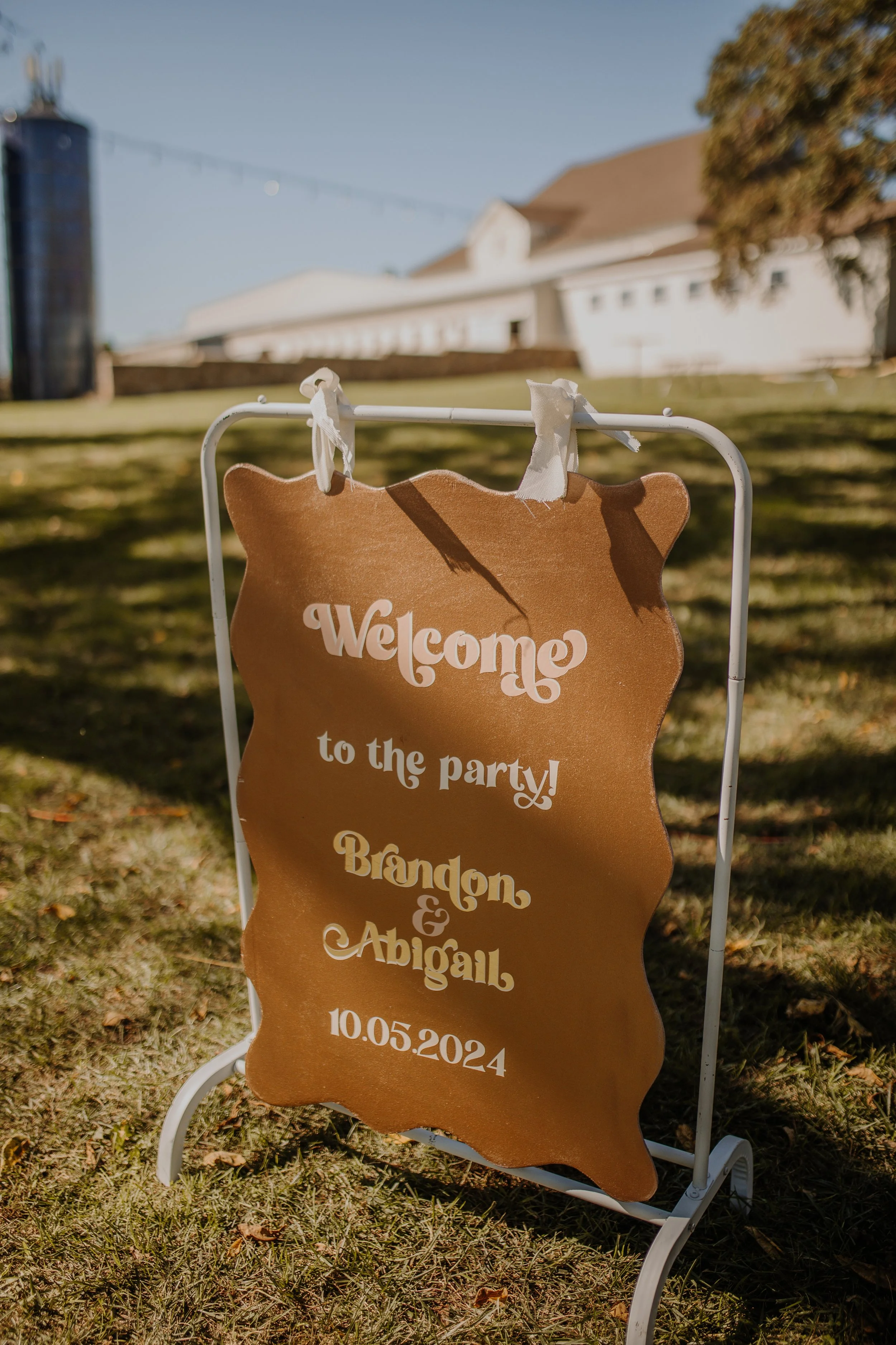 Welcome sign for Brandon and Abigail's wedding party with date October 5, 2024, on an outdoor lawn.