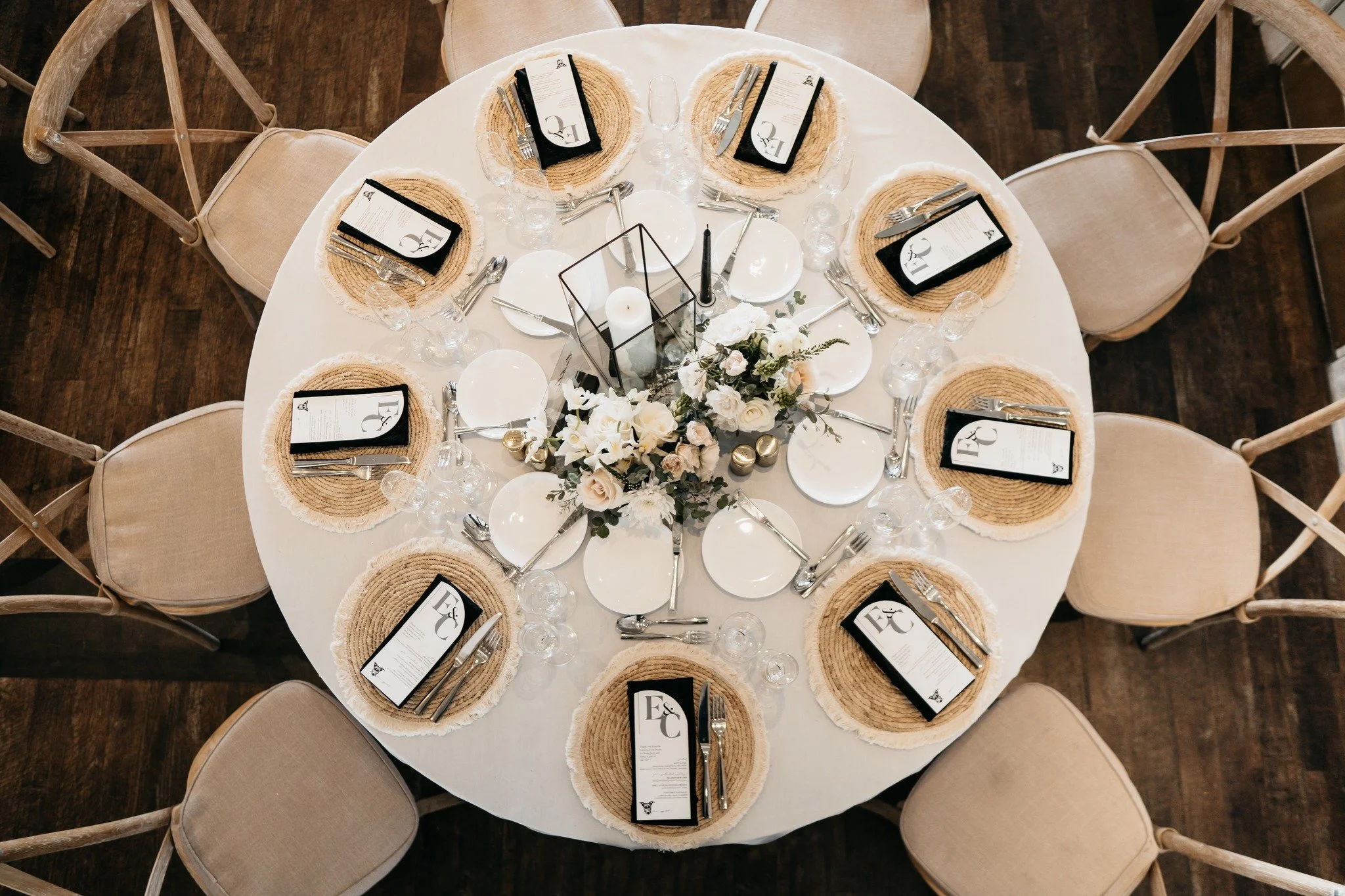 Round table set for a formal event with eight place settings, a floral centerpiece, candles, and napkins with menus.