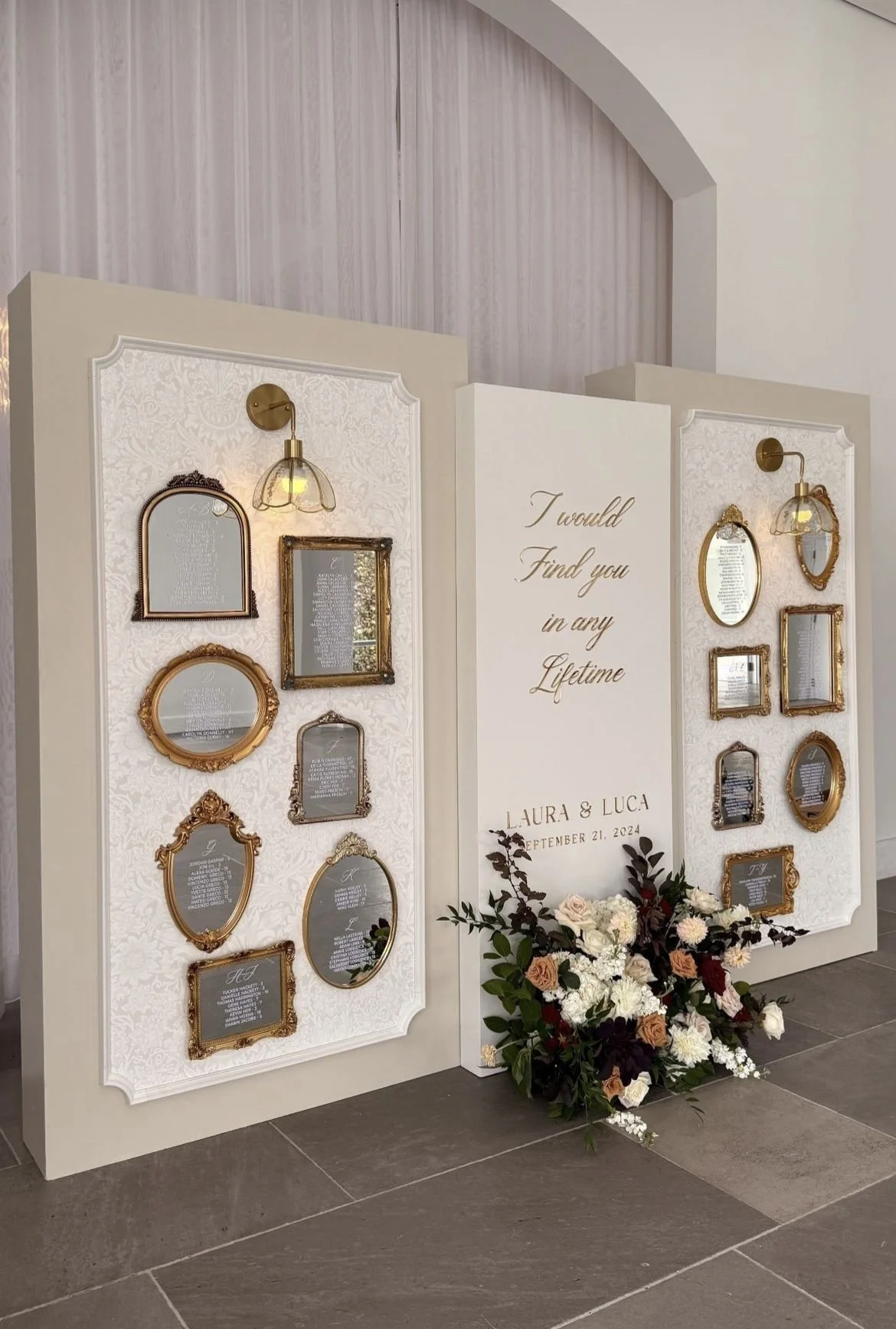 Decorative wedding seating chart with ornate picture frames and a floral arrangement beneath a large sign reading "I would Find you in any Lifetime" for Laura & Luca, September 21, 2024.