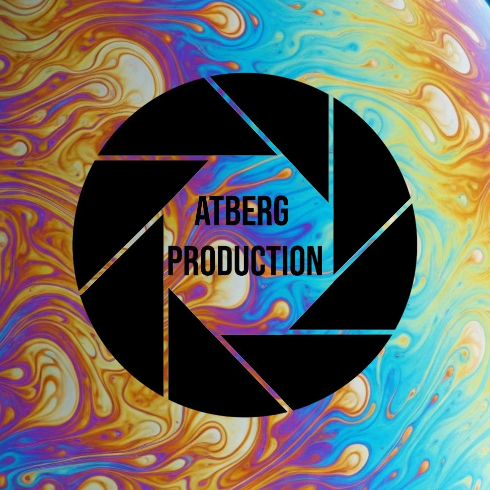 Ein abstraktes Hintergrundbild mit bunten, fließenden Farben in Blau, Gelb, Orange und Lila. Im Mittelpunkt ein schwarzer Kreis mit einem Fotoknopf-Symbol. Darin steht in schwarzen Buchstaben 'ATBERG PRODUCTION'.