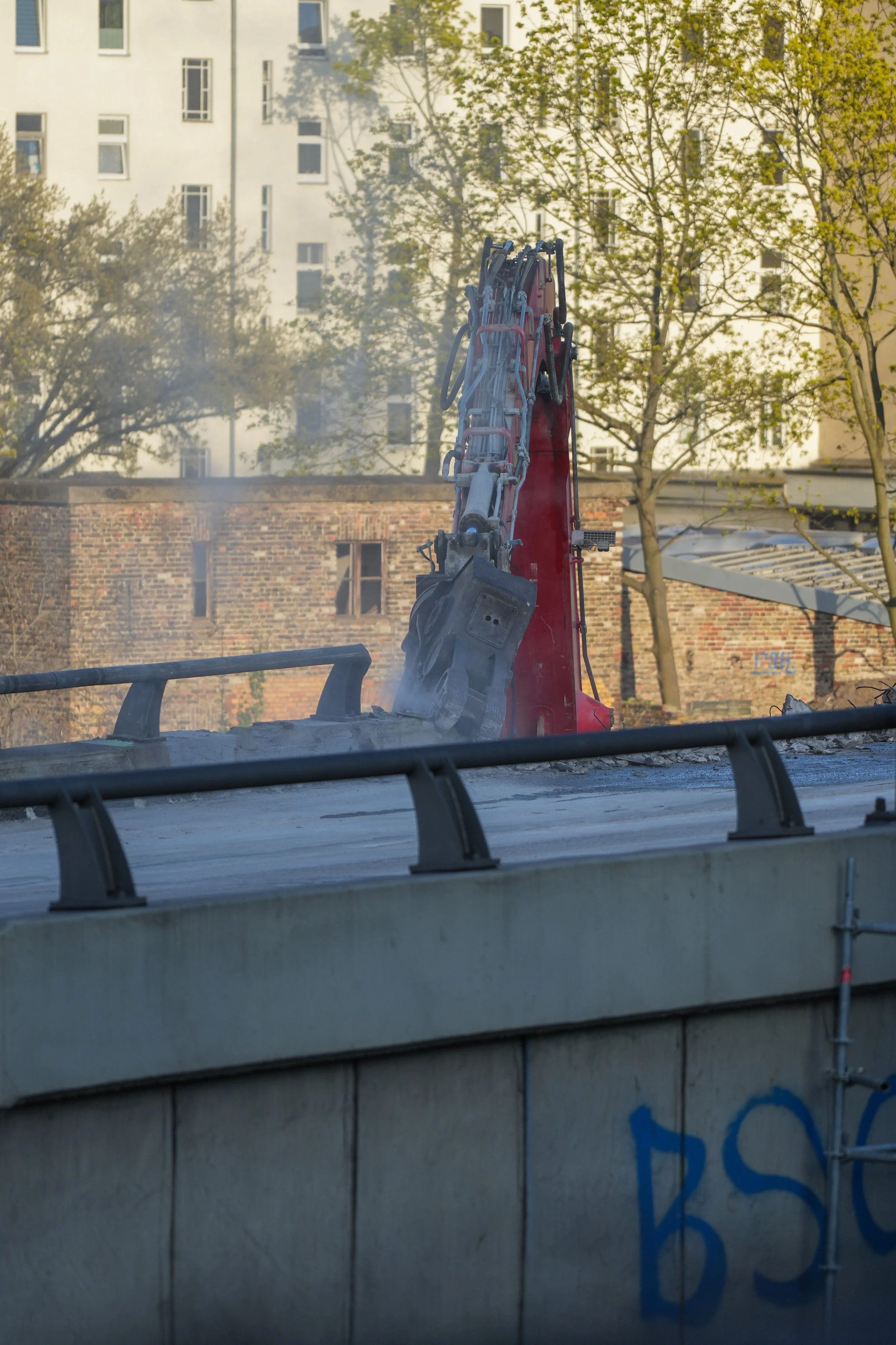 Baumaschine auf Brücke während Abrissarbeiten mit Gebäude im Hintergrund.