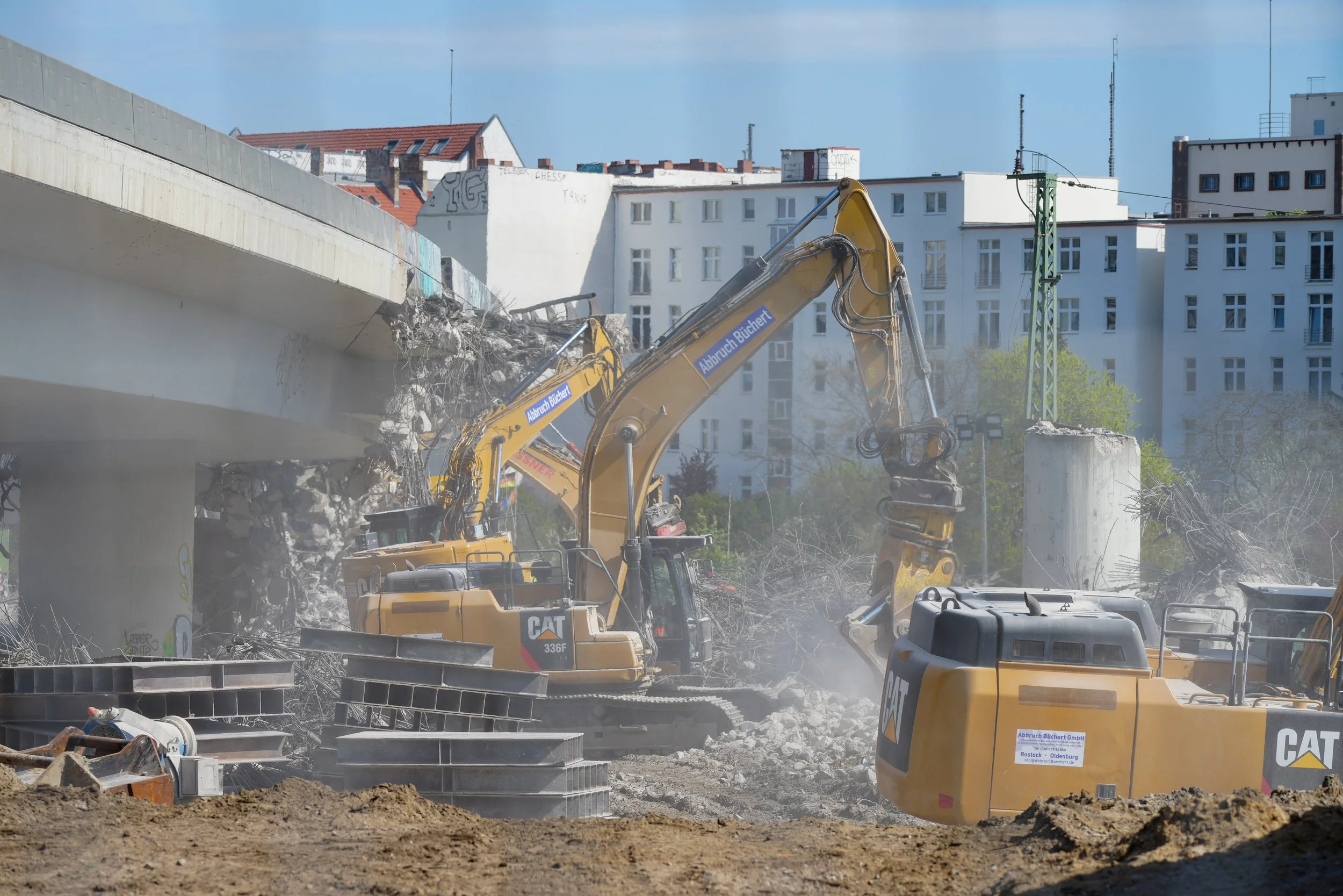 Abbrucharbeiten an einer Brücke mit mehreren Baggern, die Beton und Stahlträger entfernen, im Hintergrund Wohngebäude.