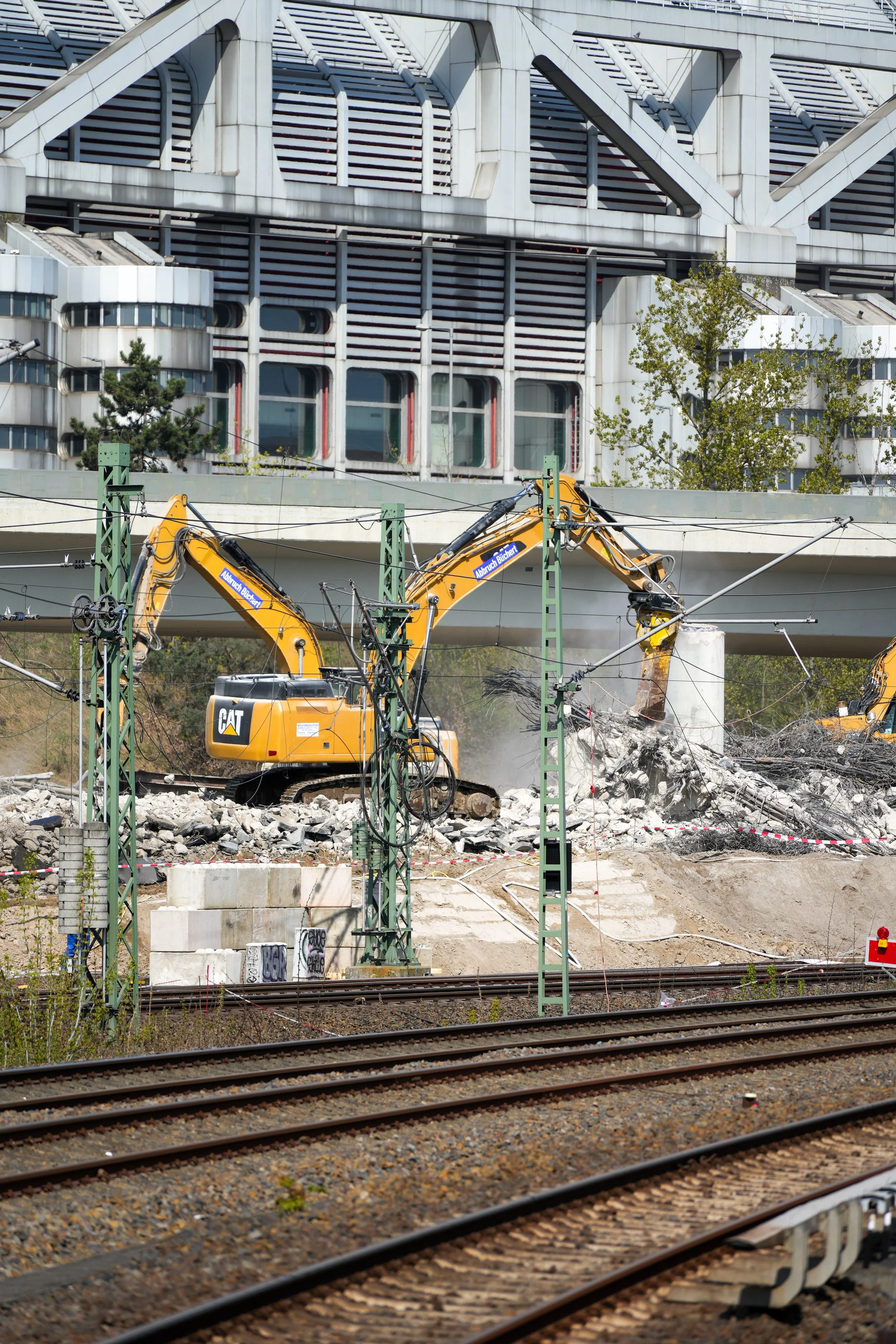Zwei gelbe Bagger bei Abbrucharbeiten auf einer Baustelle neben Bahngleisen.