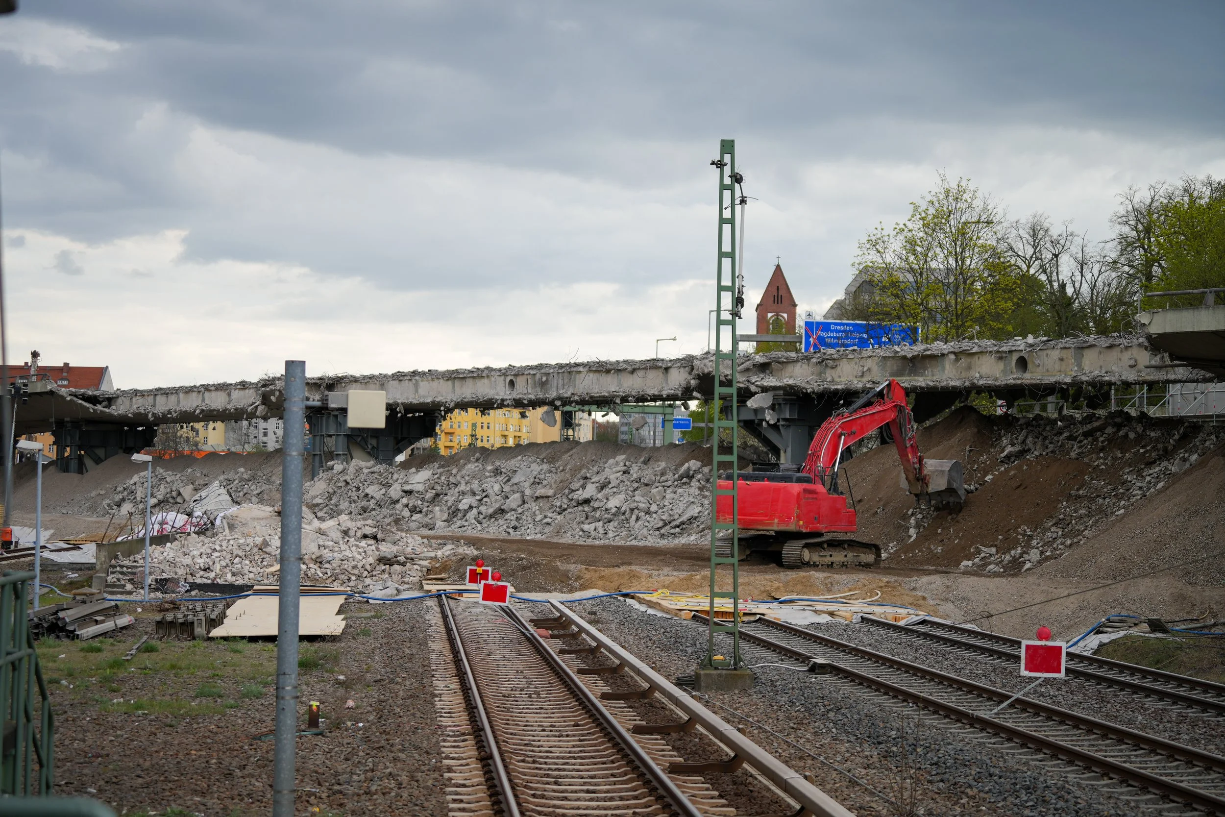 Abbruch einer Brücke über Eisenbahnschienen mit einem roten Bagger auf einer Baustelle.