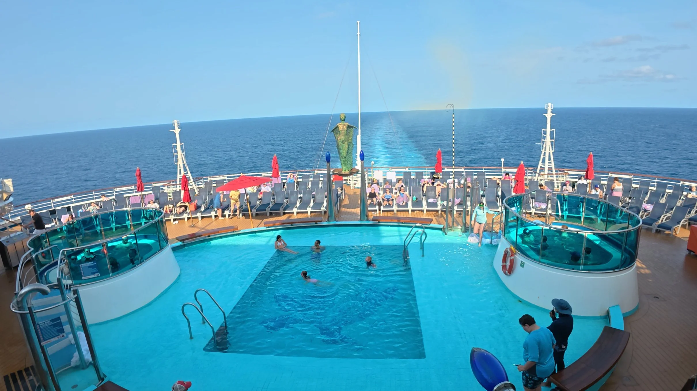 Cruise ship pool deck on a sea day with passengers relaxing in chairs and pools