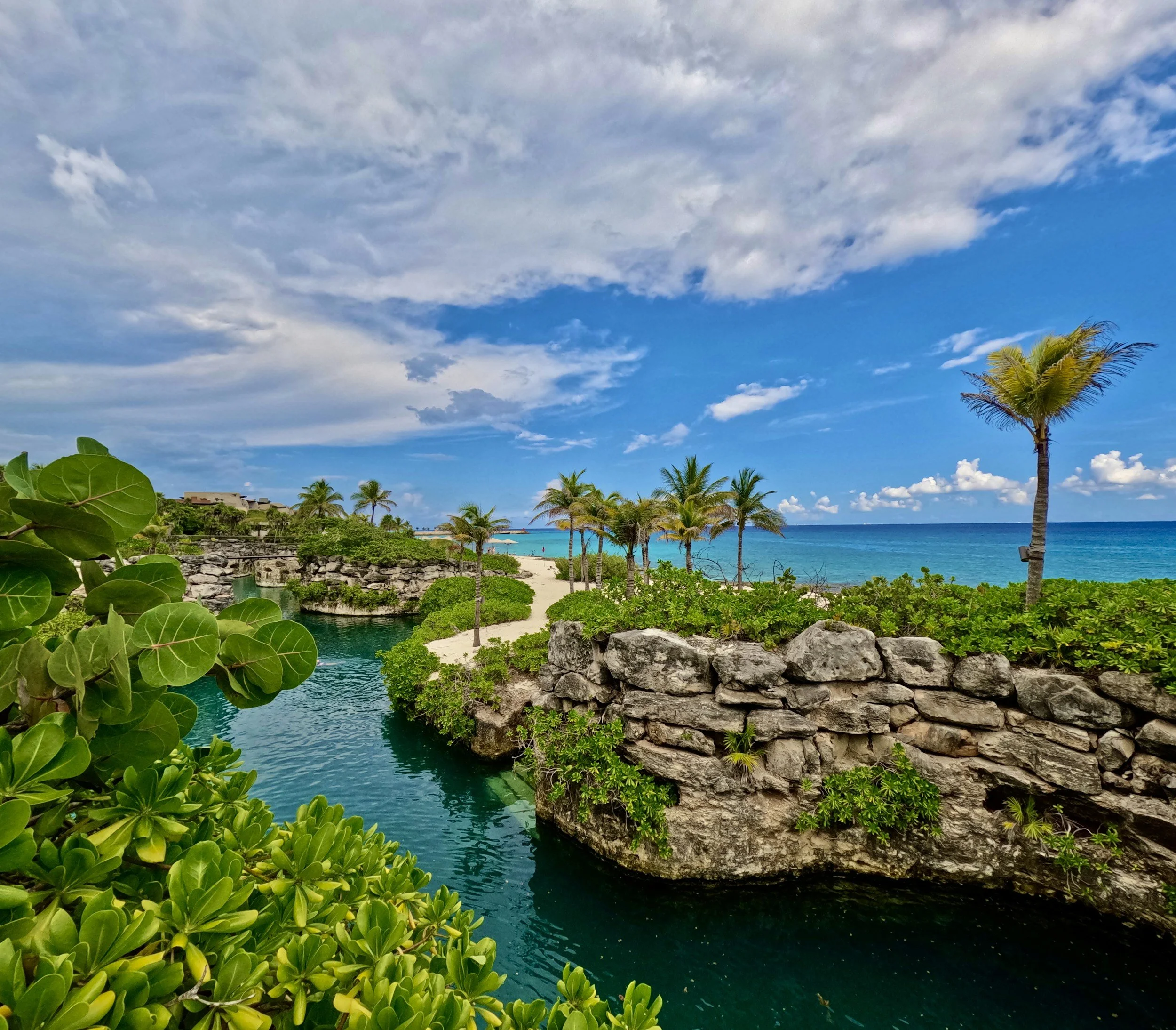Ocean view with turquoise lagoon, rocky shoreline, and palm trees at Hotel Xcaret Mexico in Riviera Maya Mexico