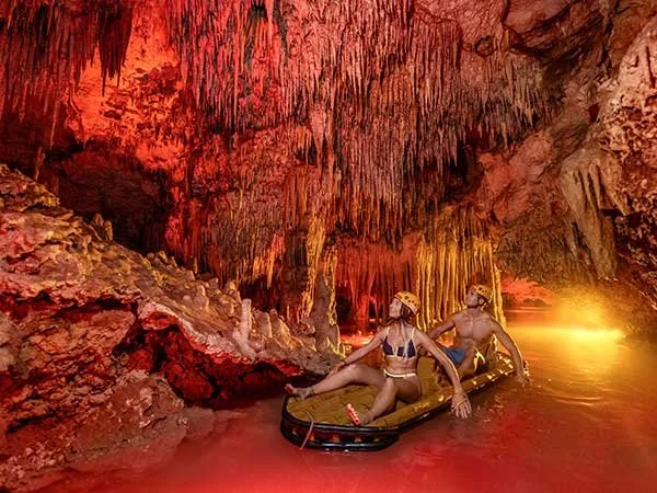Guests floating through a fire-lit underground river cave at Xplor Fuego night adventure park in the Riviera Maya.