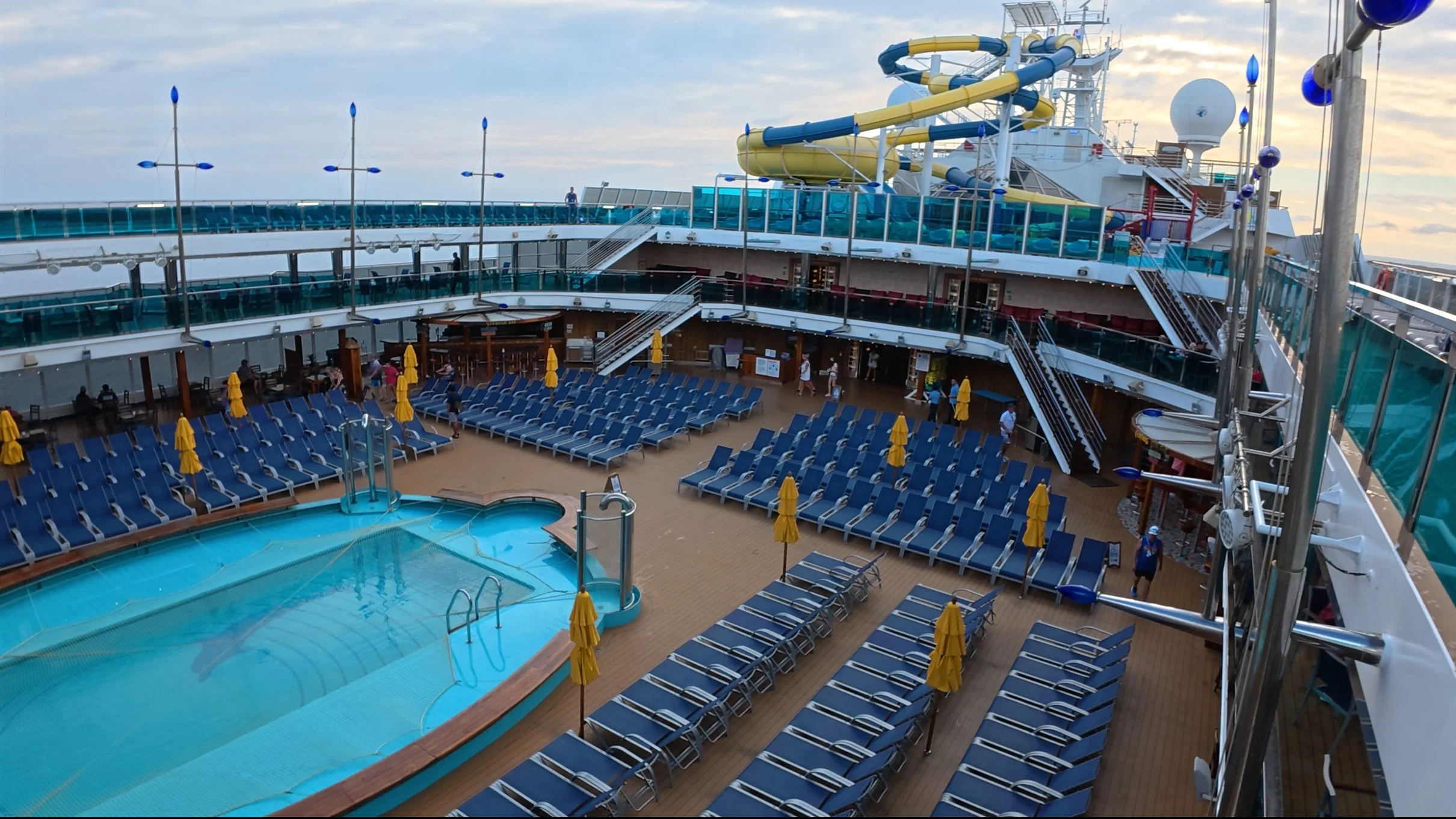 Carnival Cruise Lido Deck with lounge chairs, pool area, and colorful water slides in the background.