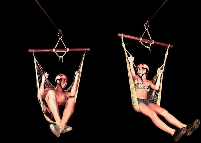 Guests riding hammock-style zipline splashes at night during Xplor Fuego’s after-dark adventure experience.