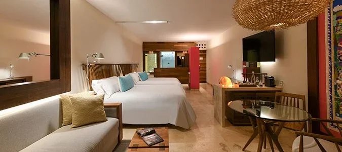 Spacious suite interior at Hotel Xcaret Mexico with king bed, sitting area, and modern natural design elements