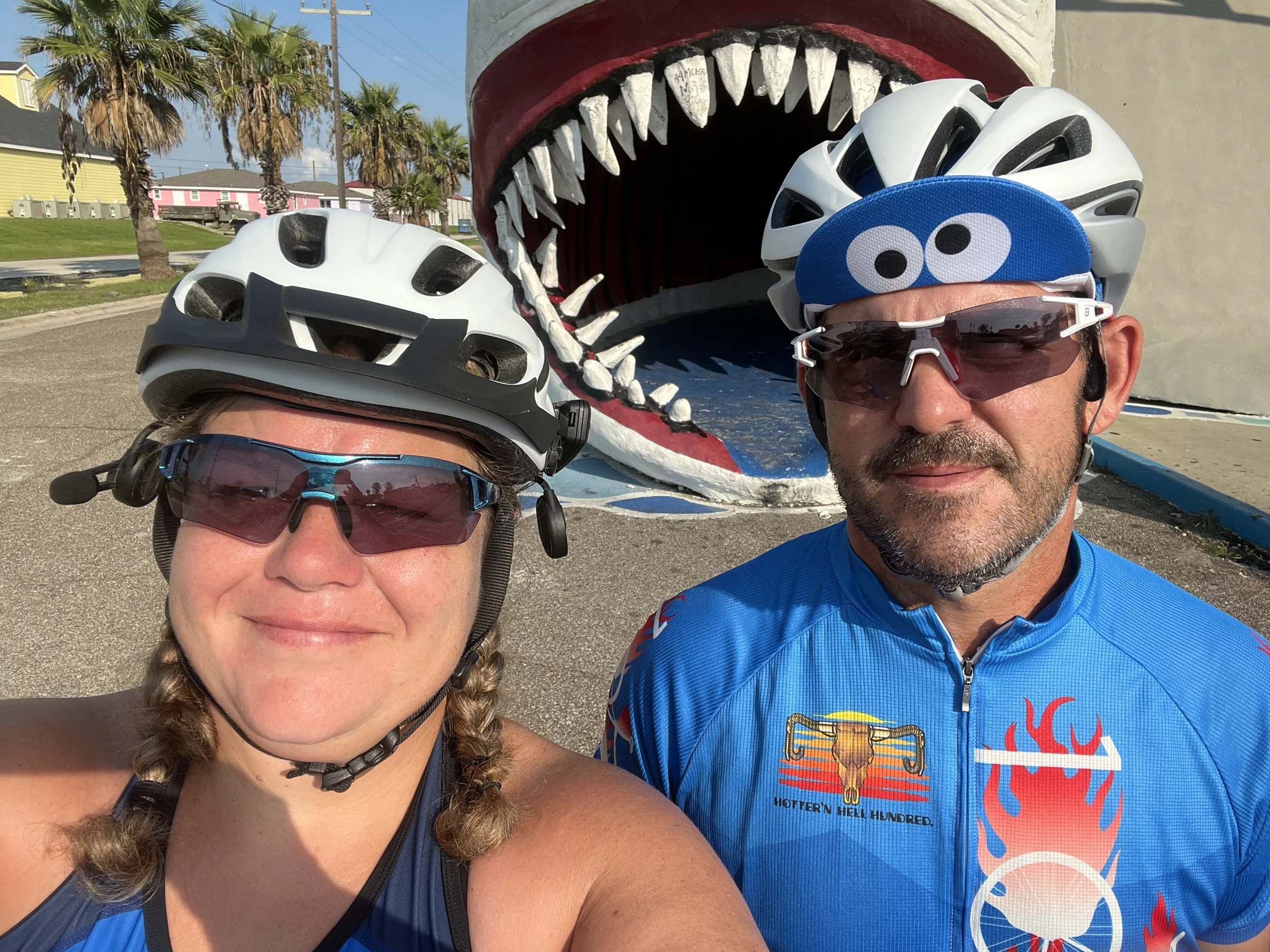 The Sea Seeker owners in cycling gear posing in front of the large shark sculpture outside a souvenir shop in Port Aransas, Texas