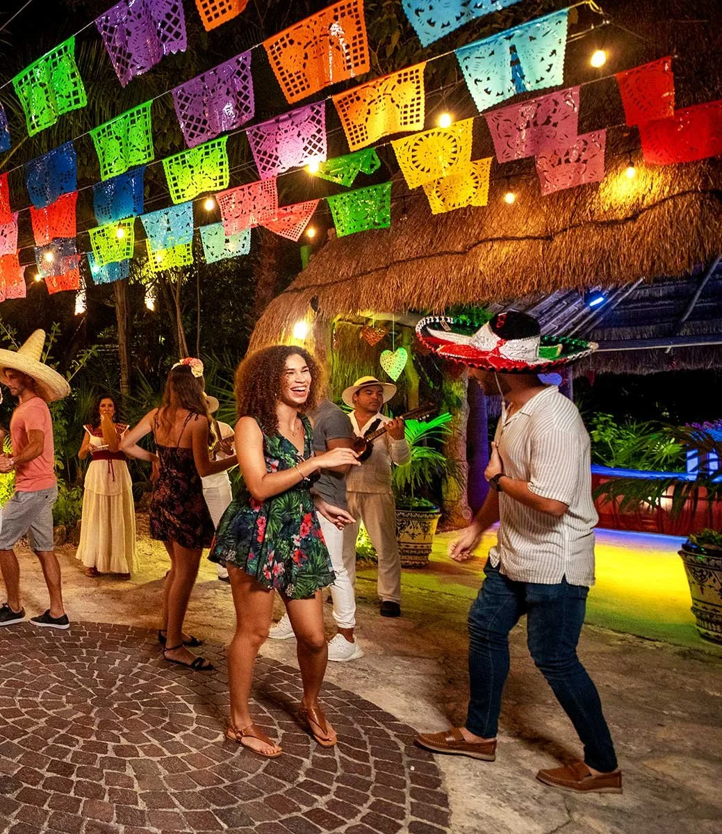 Guests dancing under papel picado during the festive Xoximilco Xcaret nighttime dinner experience.