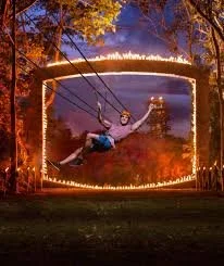 Guest ziplining at night through the jungle at Xplor Fuego, illuminated by torches and fire-lit pathways.