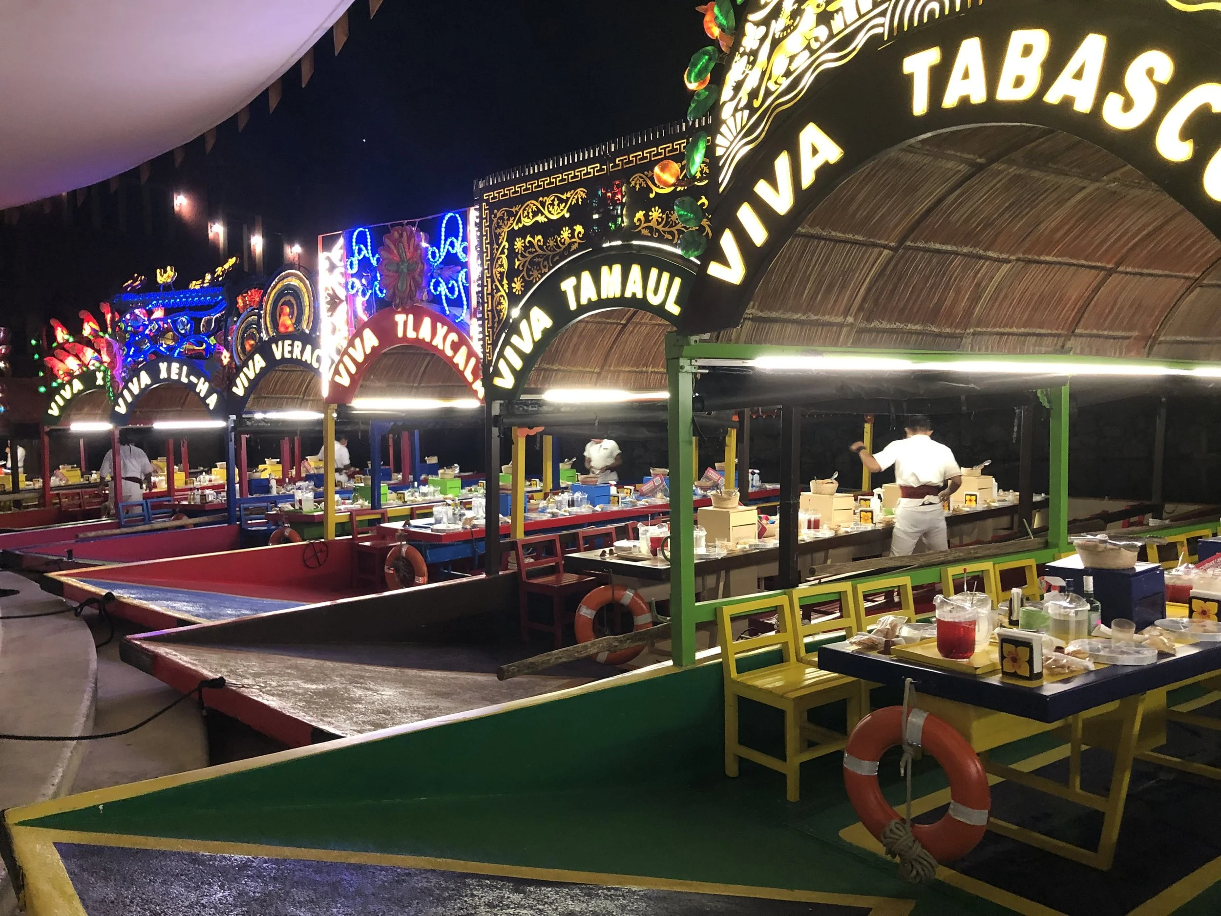 Colorful trajineras lined up at night during the Xoximilco Xcaret floating dinner party experience.