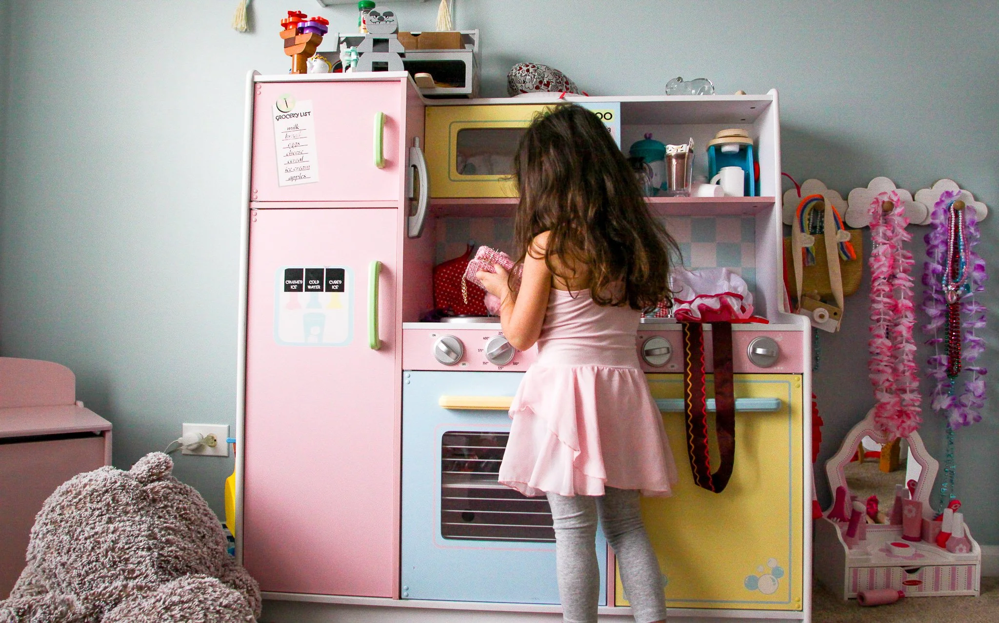 A young girl with curly hair is playing with a toy kitchen set in a child's room that is decorated with pastel colors and accessories.