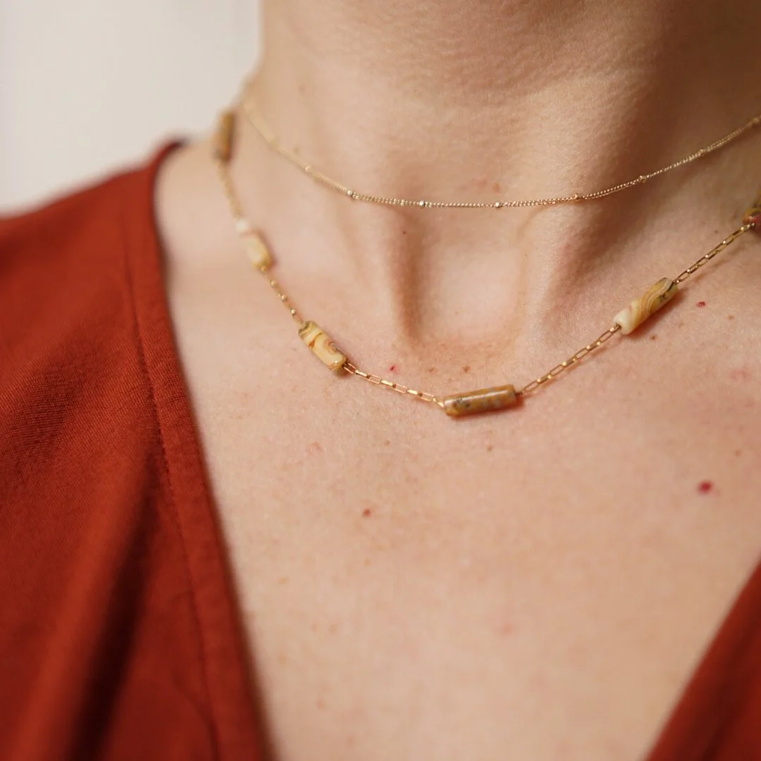 Woman wearing a gold filled station necklace with crazy lace agate tube beads, layered with a delicate satellite chain, in a rust red top