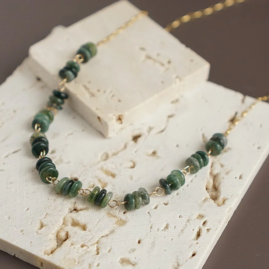 Green moss agate rondelle bead necklace with 14k gold filled chain resting on cream travertine display blocks