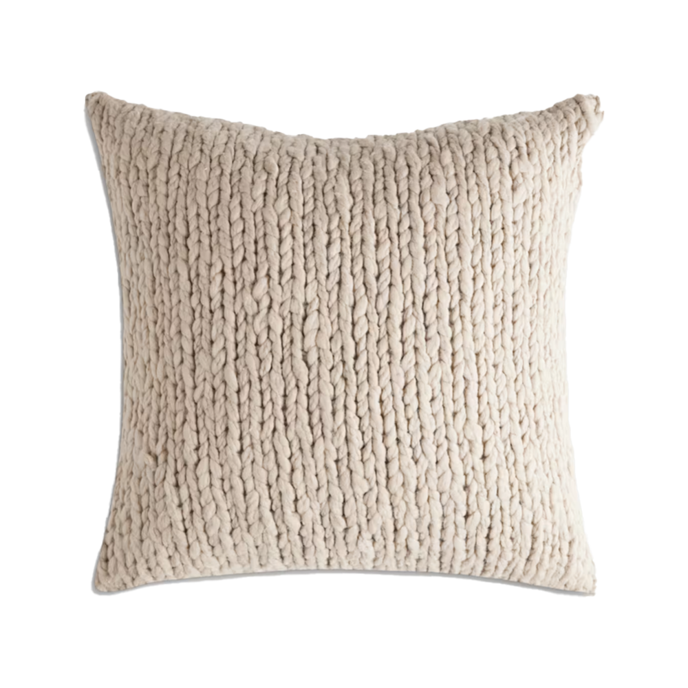 A square beige knitted throw pillow with chunky braided texture.