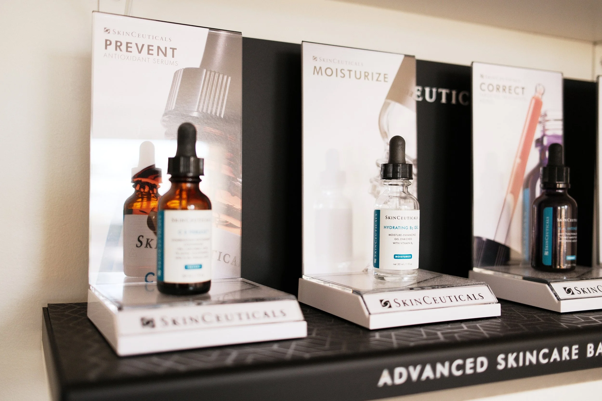Display of SkinCeuticals skincare products, including antioxidant serums and moisturizing gel, on a black shelf with branded packaging and labels.