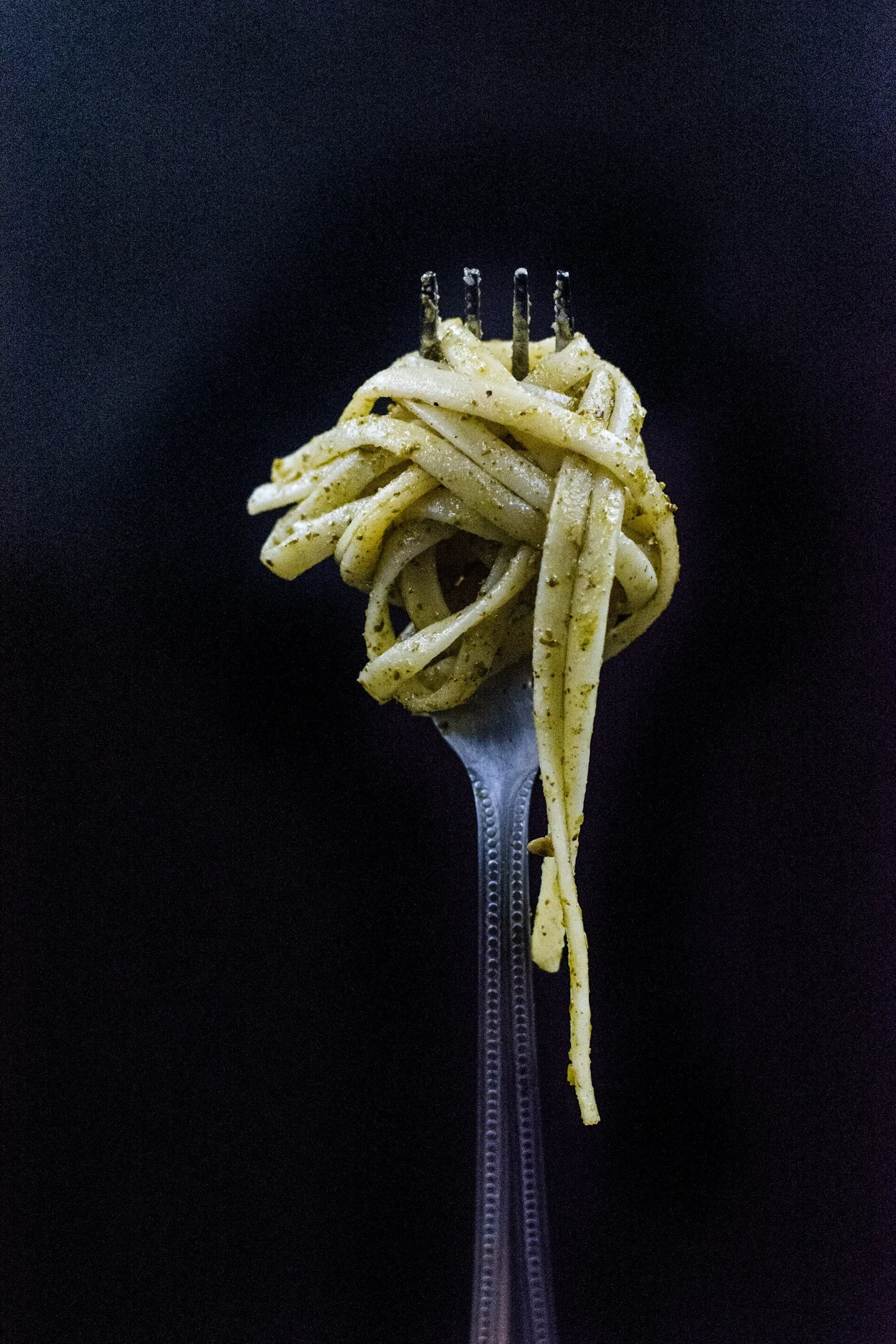 Fork with a serving of spaghetti pasta topped with black pepper, held against a black background.