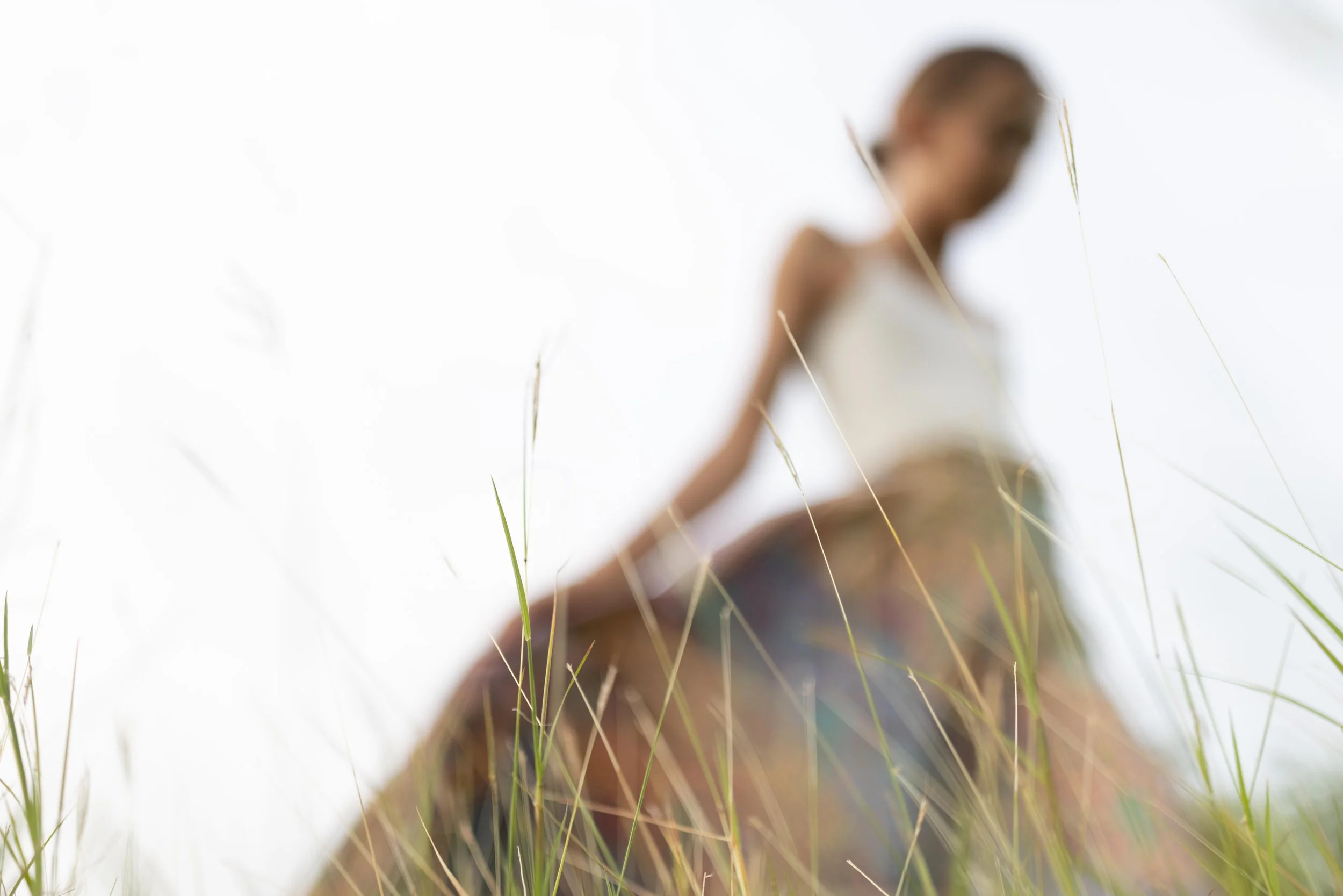 Blurred image of a girl riding a horse in a grassy field, with tall grass in the foreground.