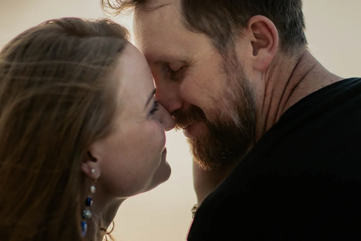 A close-up of a couple touching foreheads, smiling with eyes closed, in an intimate moment.
