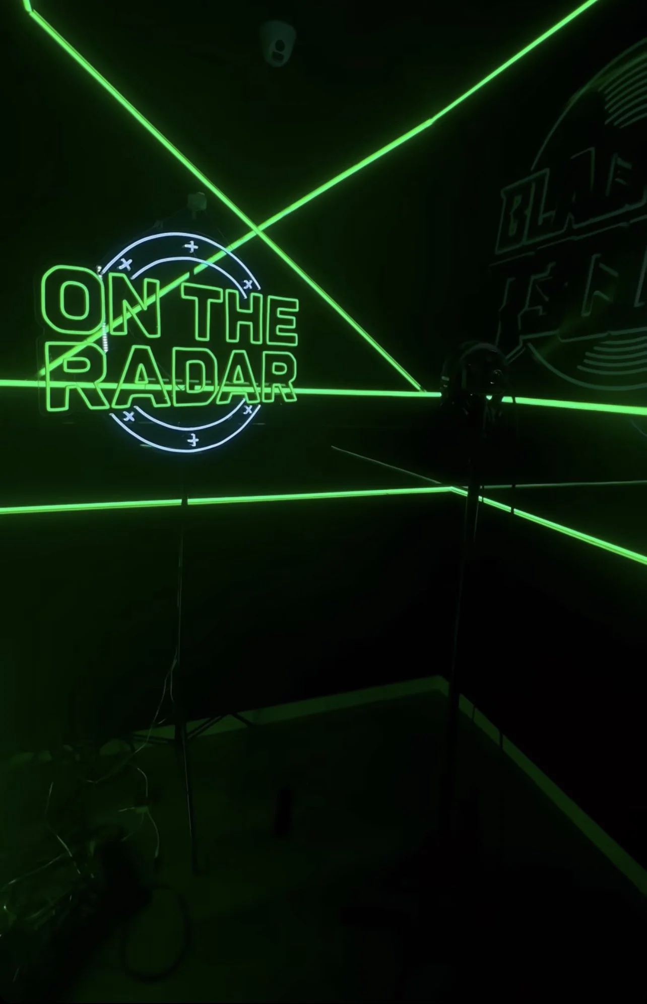 Dimly lit studio with green neon lighting featuring the words 'On The Radar' and geometric line designs on walls.