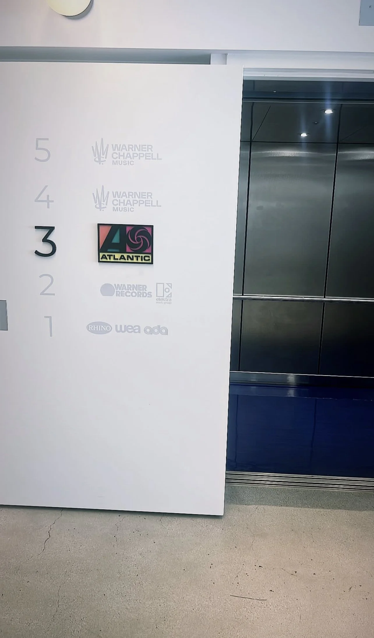 Elevator area with floor directory, featuring various music company logos including Warner Chappell Music, Atlantic, and Warner Records.