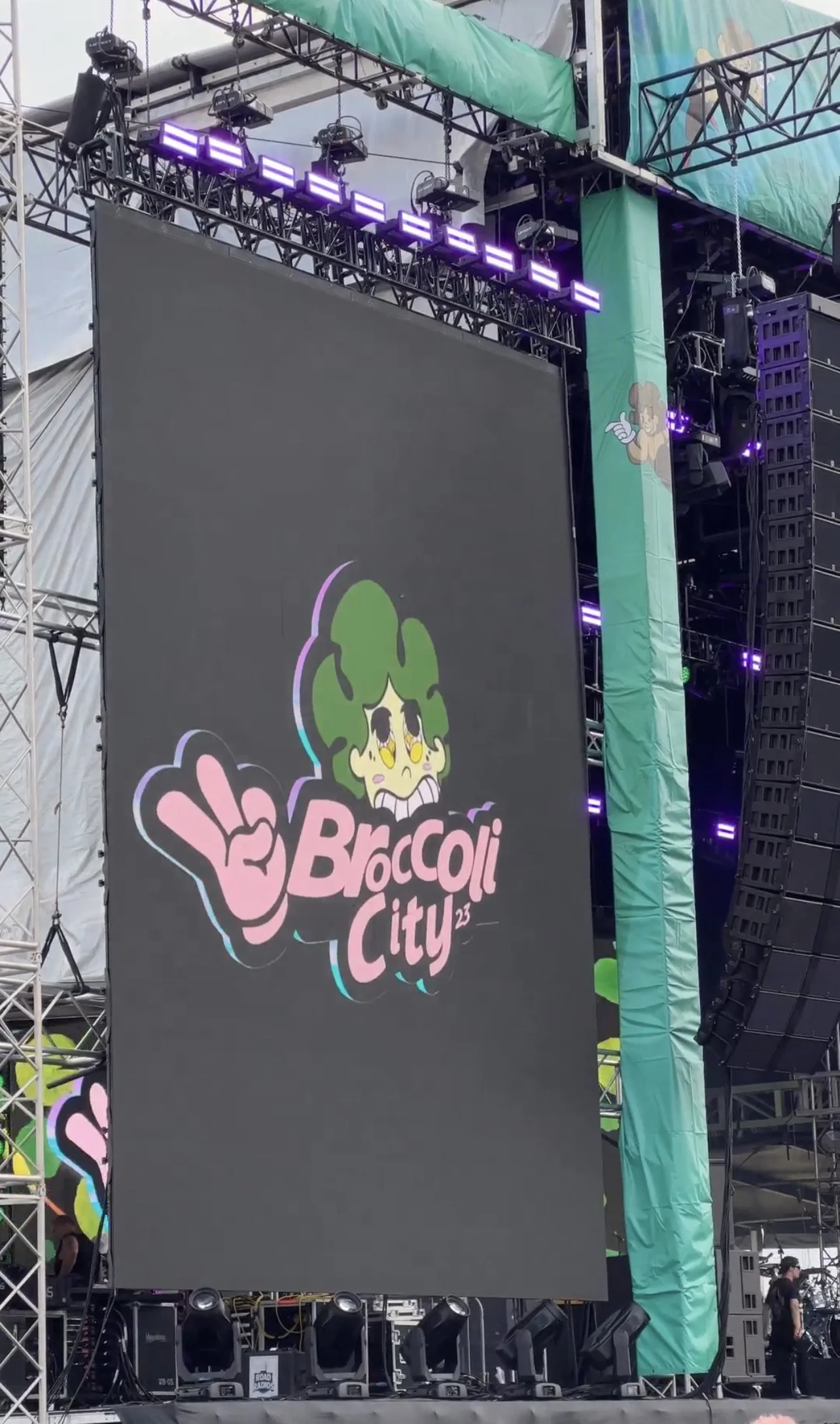 Large outdoor stage with a screen displaying the Broccoli City 2023 logo, featuring a cartoon character with broccoli hair and a peace sign.