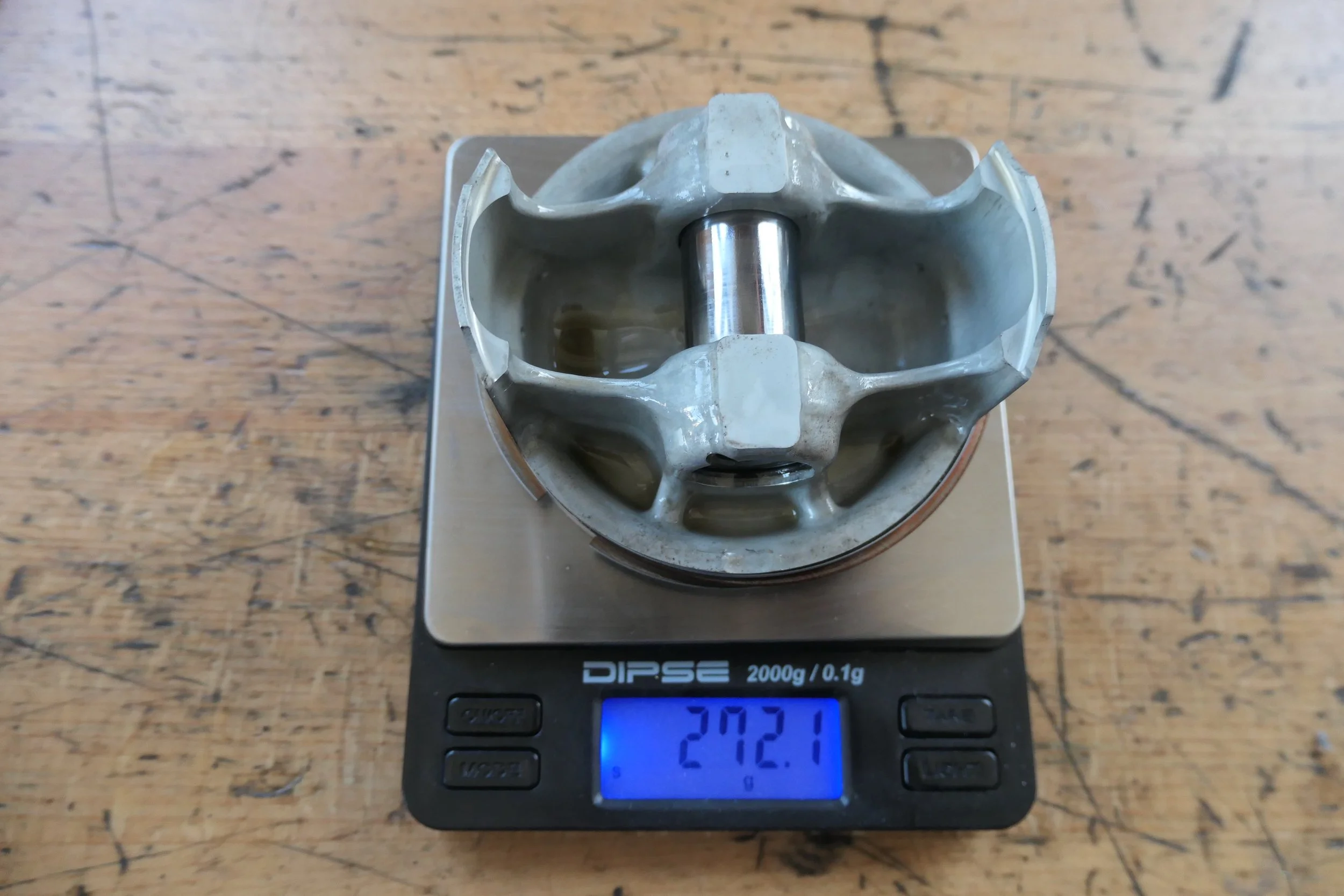 Ein Motorzylinderkopf auf einer digitalen Küchenwaage mit einem Gewicht von 272,1 Gramm, auf einem Holzarbeitsplattentisch.