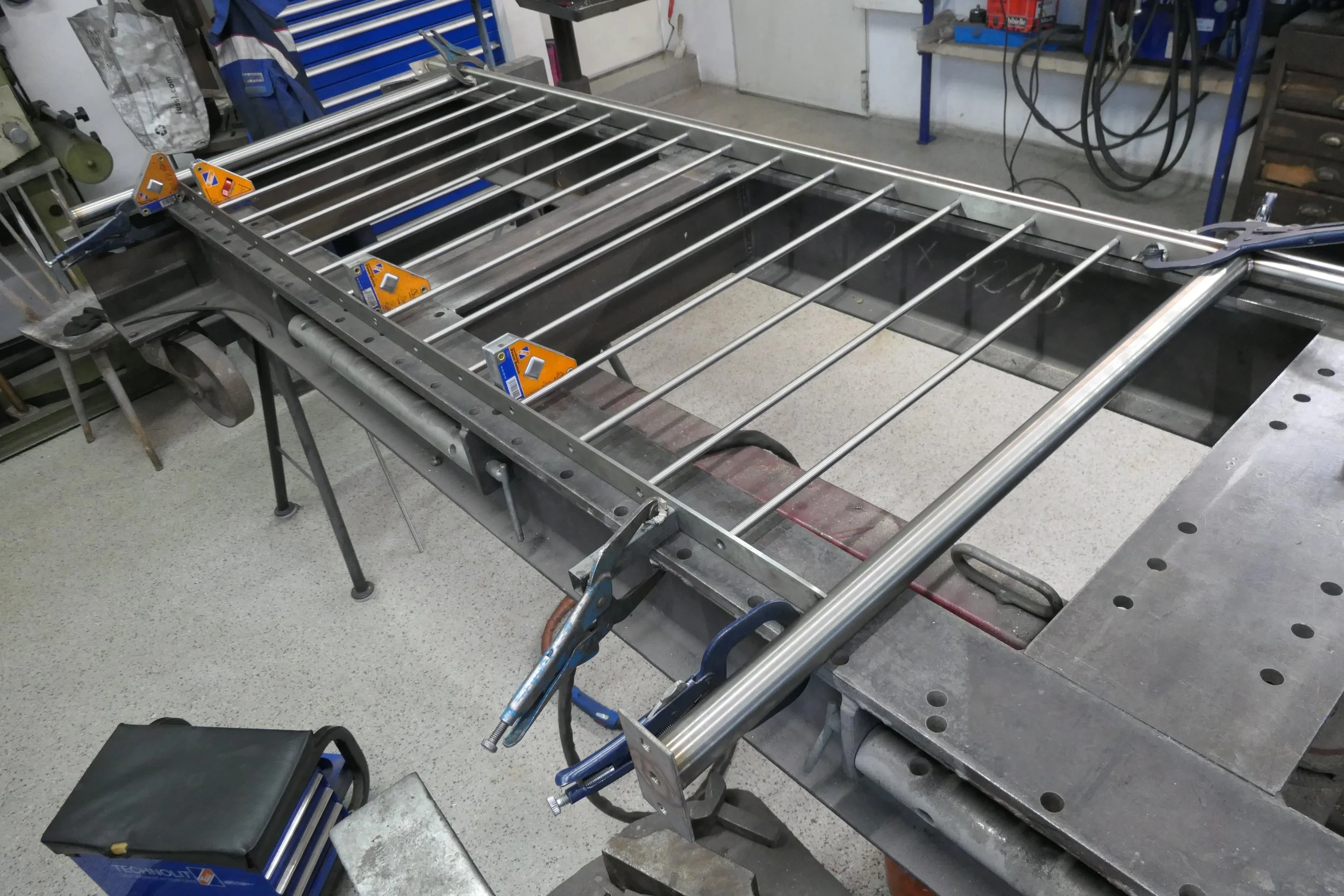 Metallrahmen mit vertikalen Metallstäben, in einem Werkstattarbeitsbereich, mit Werkzeugen und Maschinen im Hintergrund