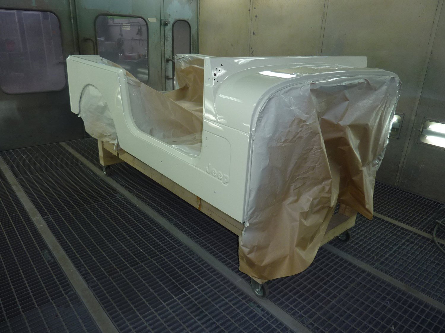 Ein Autokarosserie-Prototyp wird in einer Lackierkabine mit weißer Farbe lackiert, mit braunen Papierabdeckungen an den Seiten.