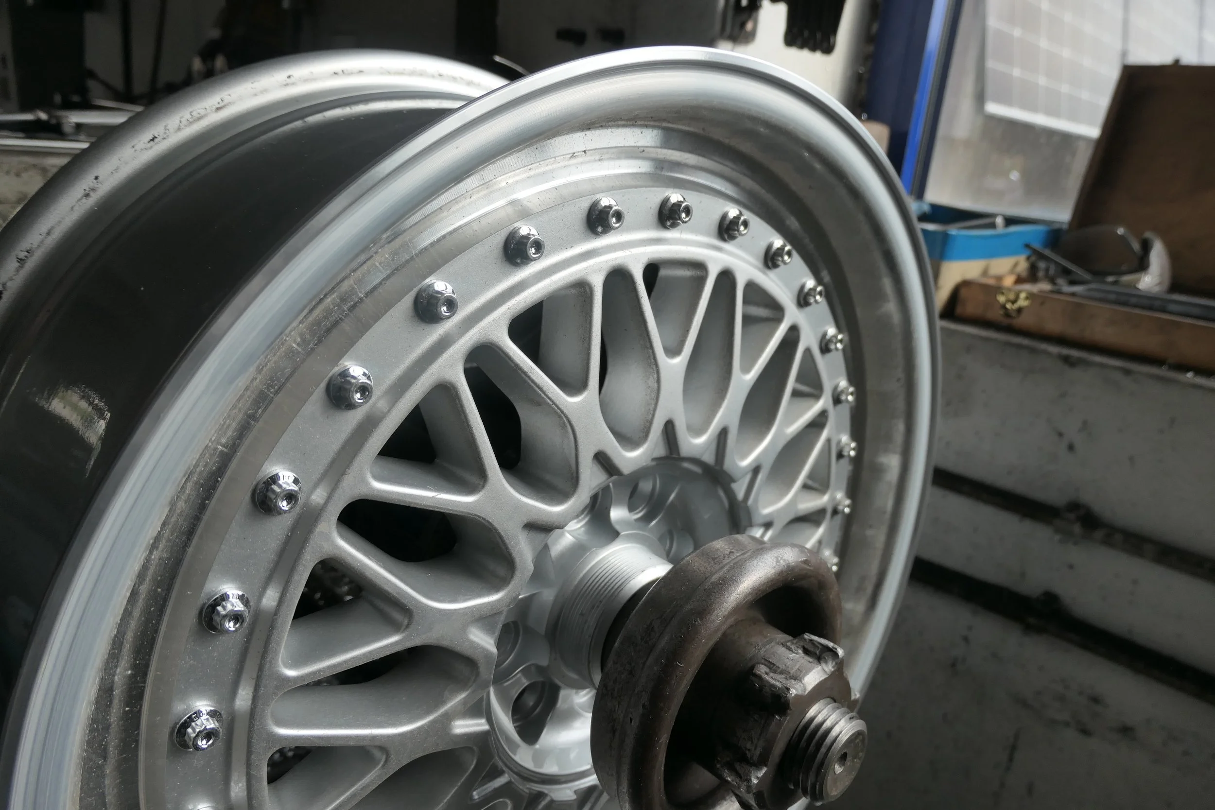 Ein Auto-Rennrad mit einem silbernen Felgendesign und mehreren kleinen Nieten um den Rand, auf einer Werkbank in einer Werkstatt.