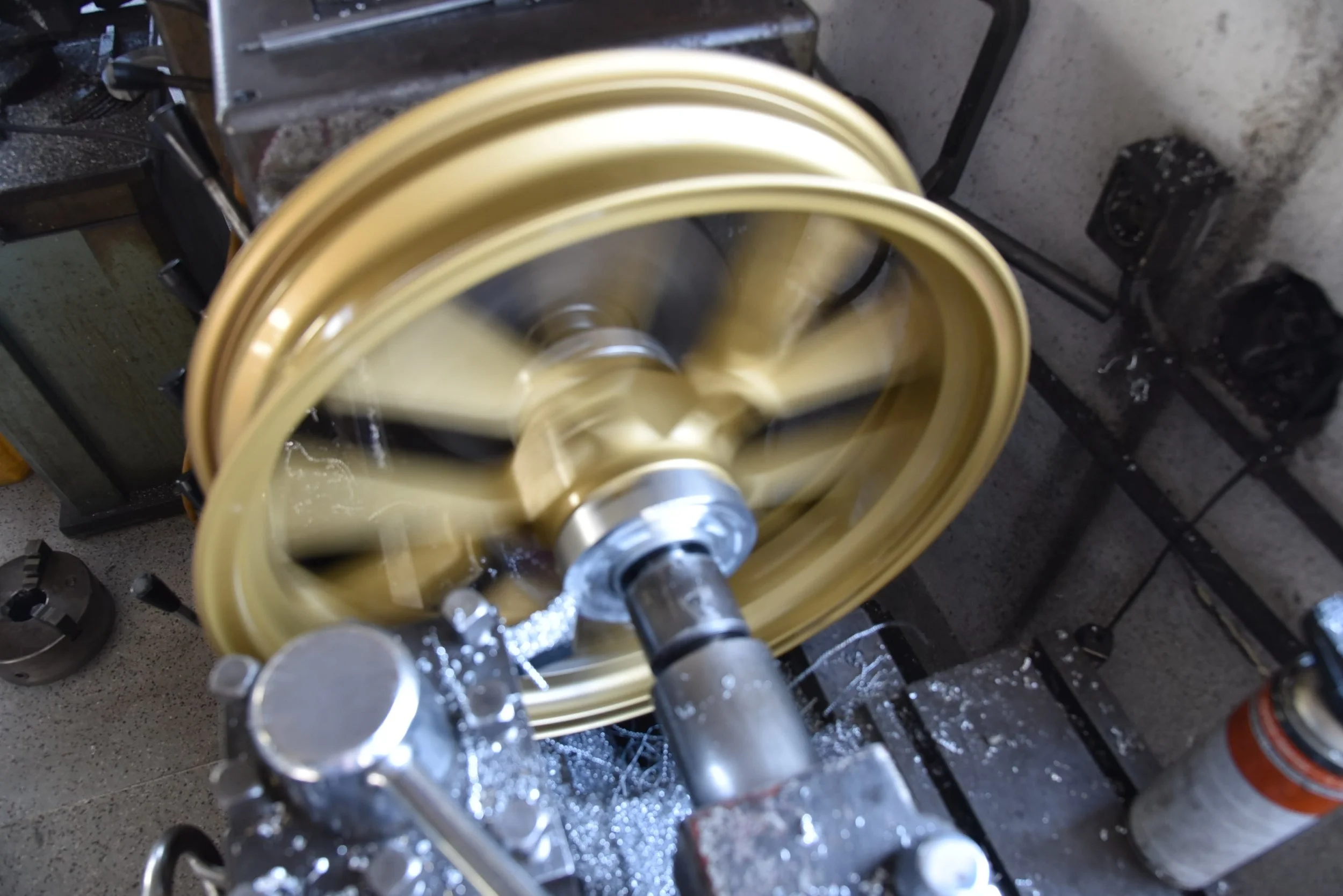 Ein goldener Metallring auf einer Maschine, die ihn dreht, während es Späne und Wasser sprüht, wahrscheinlich in einer Werkstatt