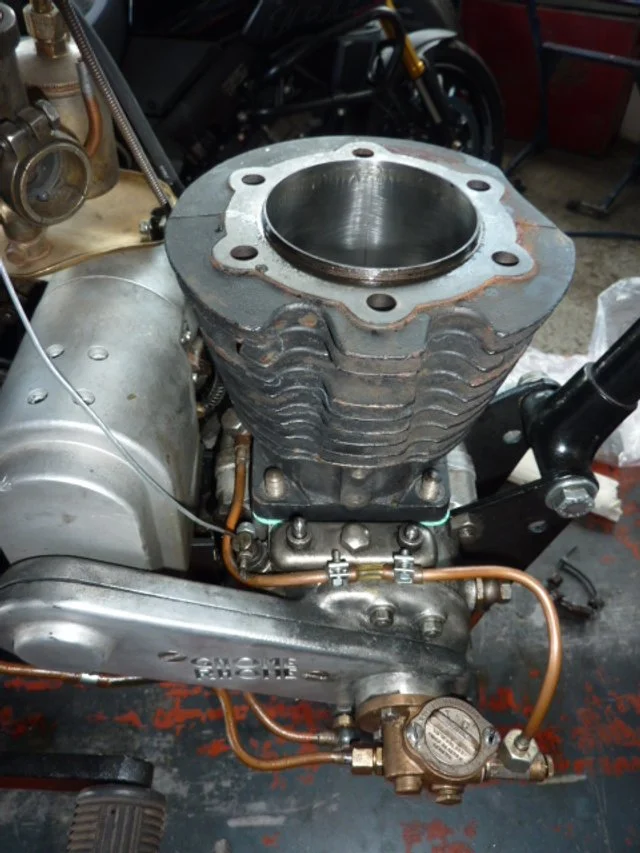 Nahaufnahme eines verbrannten, zylindrischen Motorblocks in einem Werkstatt- oder Garageumfeld.