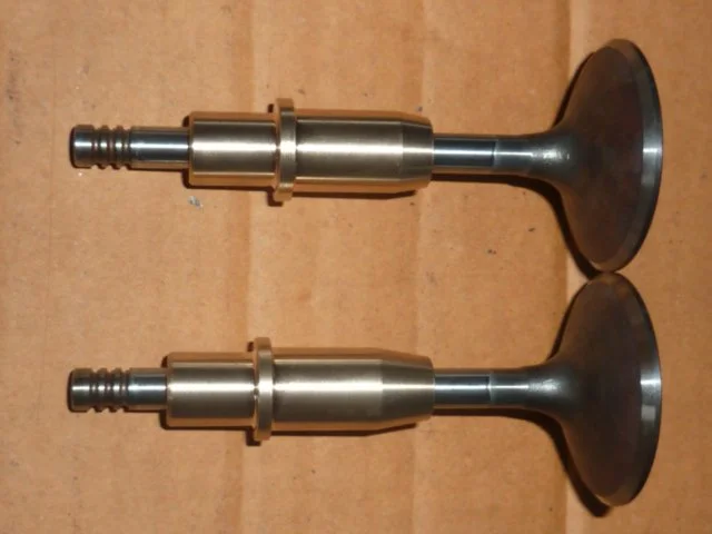 Zwei Motorventile mit runden Flanschen, aus Metall, auf einer Holzwand liegend.